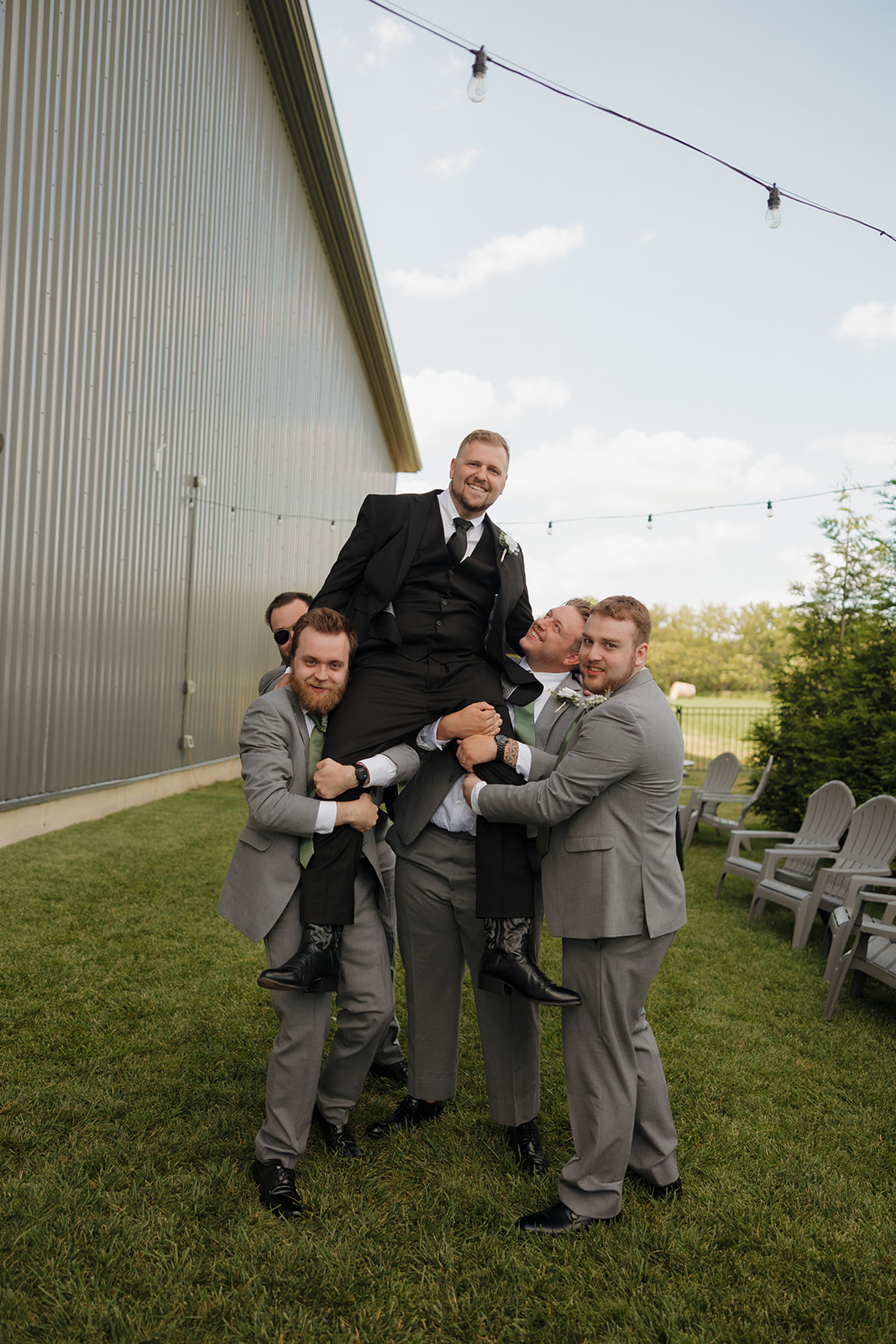 Groomsmen hoist the groom into the air for a fun pre-ceremony moment outside a Wisconsin brewery wedding venue.