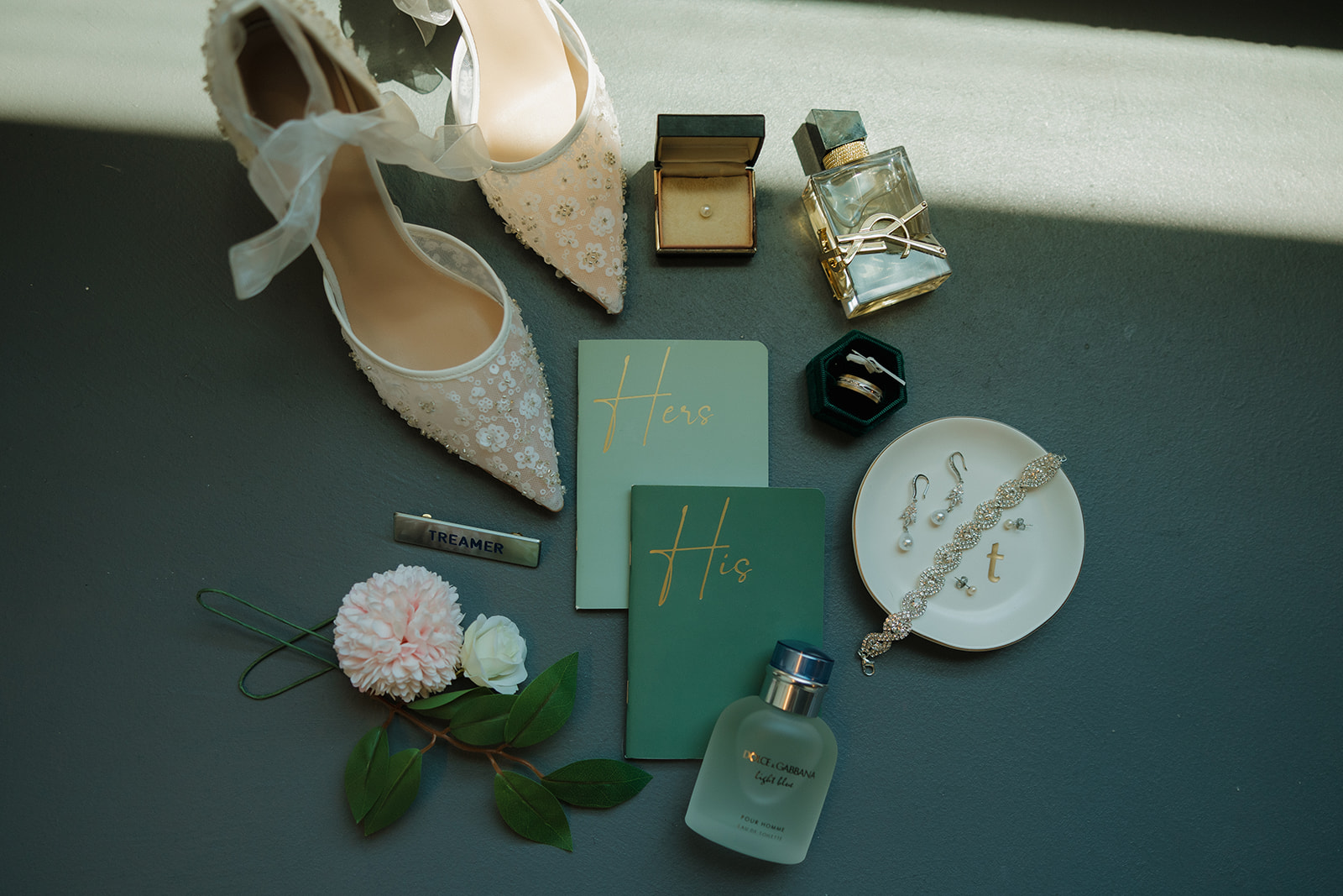 Romantic flat lay featuring embroidered bridal heels, his and hers vow books, perfume, jewelry, and florals, styled at a Wisconsin brewery wedding.
