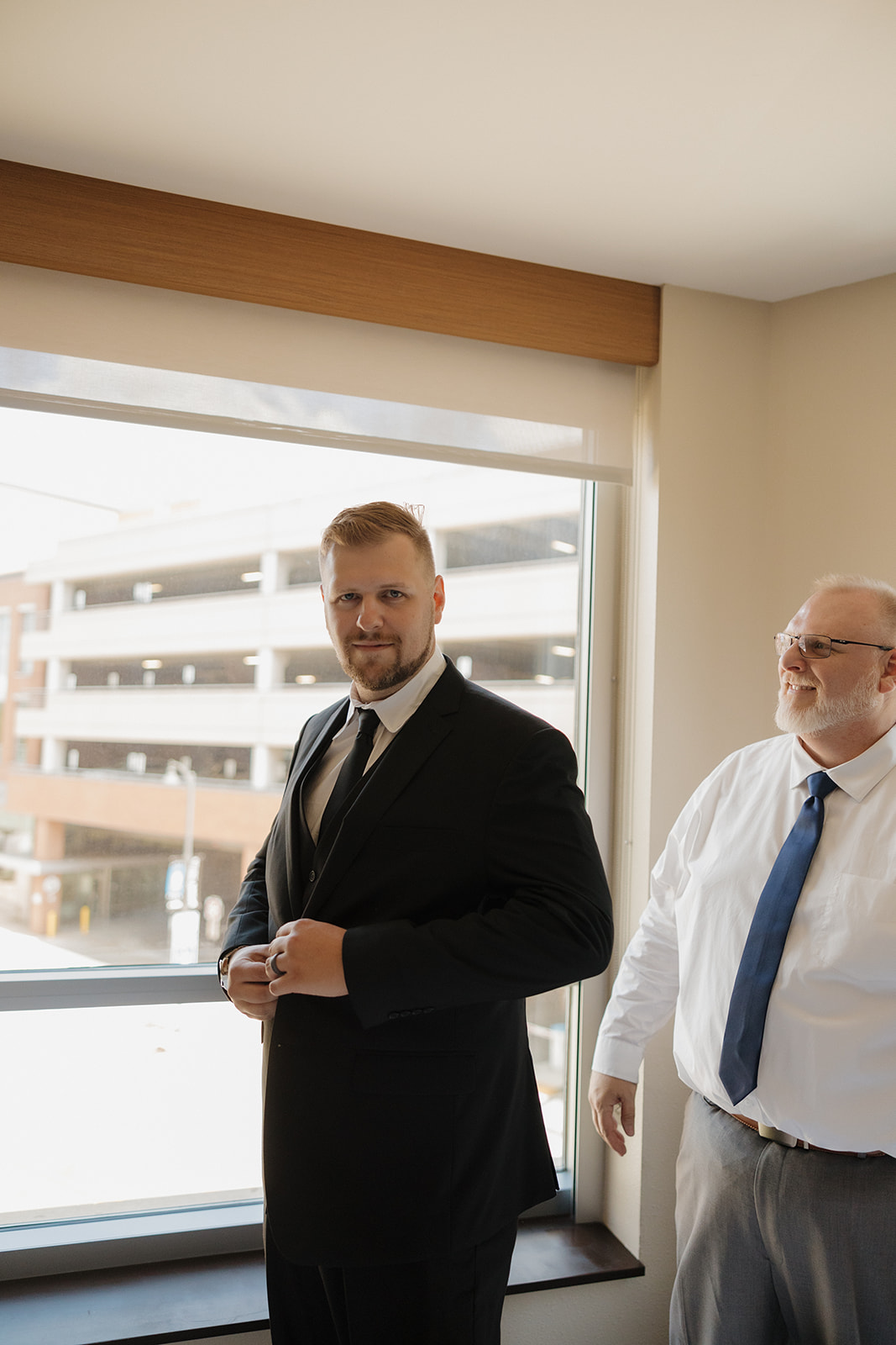 Groom adjusts his cufflinks with a proud smile as his father looks on, captured in a quiet pre-ceremony moment before his Wisconsin brewery wedding.