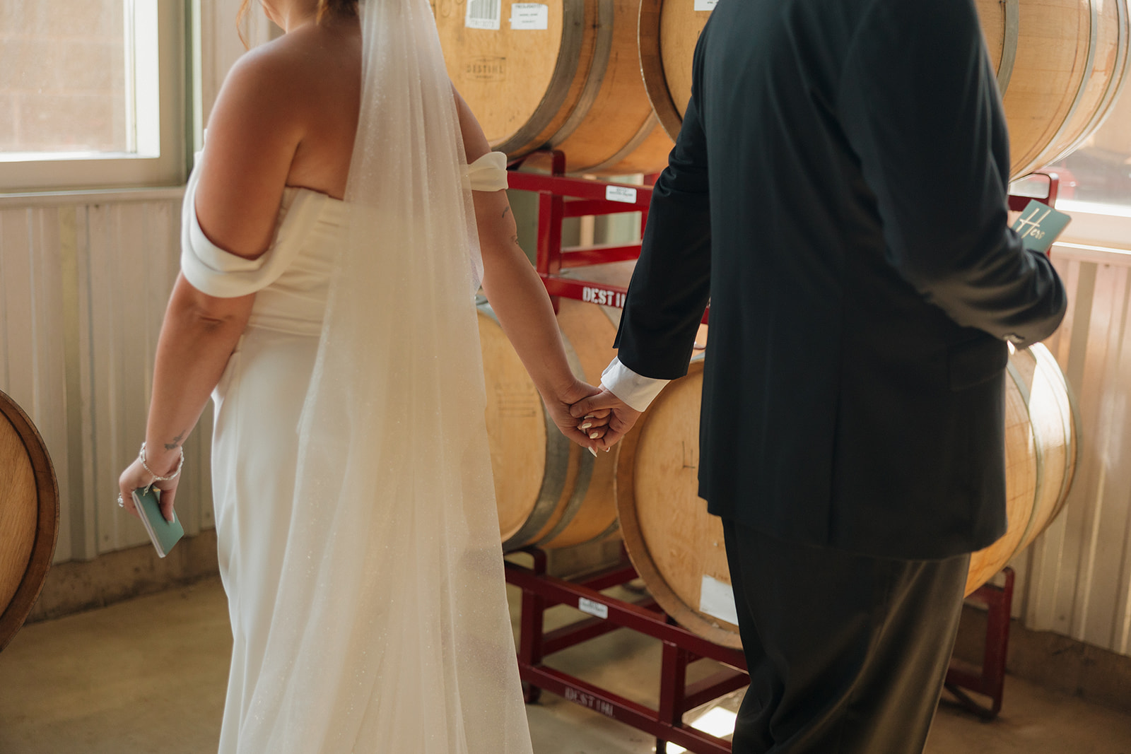 Bride and groom hold hands around a corner for a sweet first touch, sharing private vows before the ceremony at a Wisconsin brewery wedding.