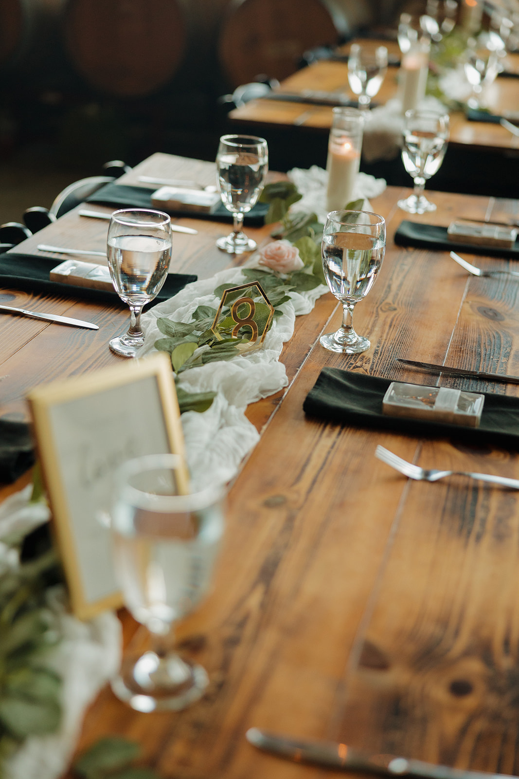 Wooden reception tables styled with greenery runners, glassware, candles, and soft florals for a rustic-chic Wisconsin brewery wedding.