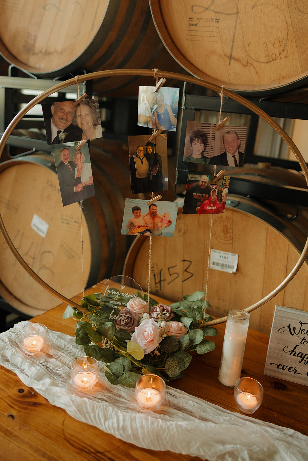 A sentimental memorial table with framed photos, flowers, and candles set against brewery barrels at a Wisconsin brewery wedding.