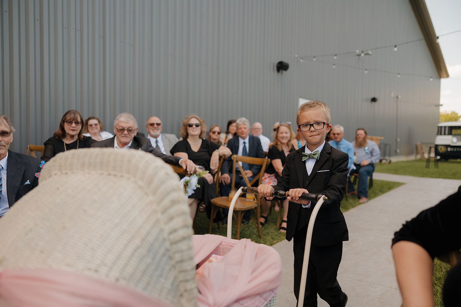 Young ring bearer in a tux pulls a baby in a wagon down the aisle as guests watch during a Wisconsin brewery wedding ceremony.