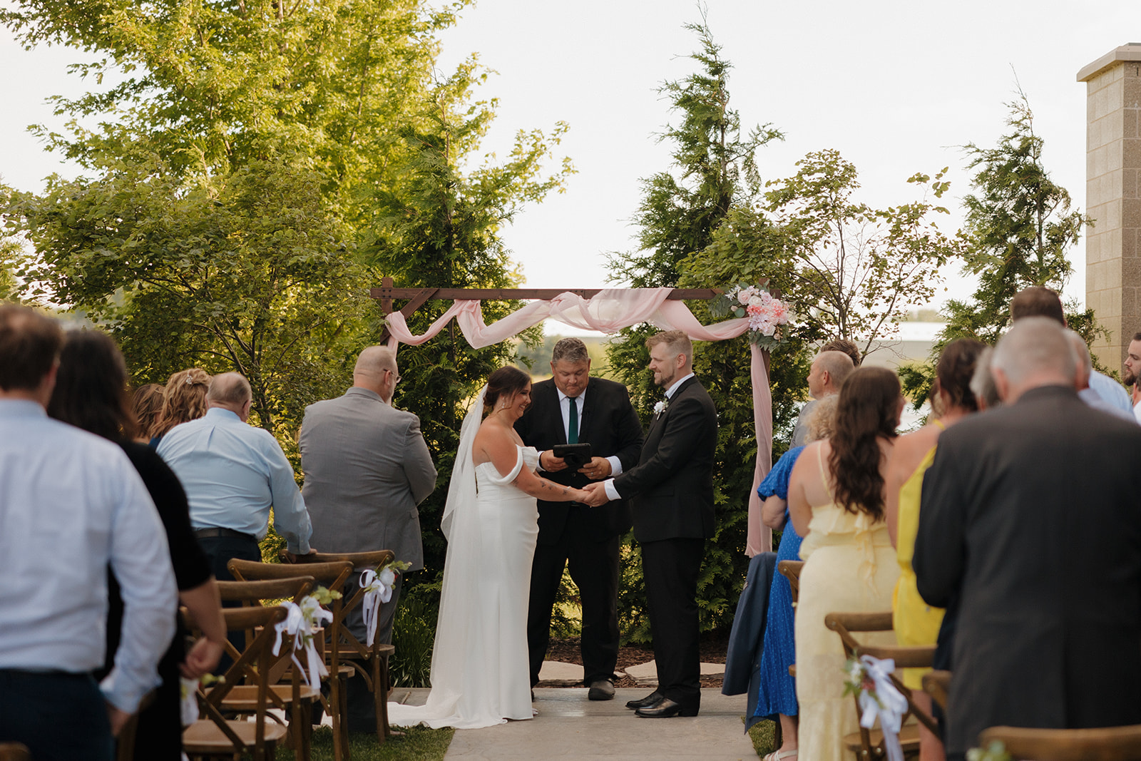 Bride and groom hold hands under a floral-draped archway during their outdoor ceremony at a Wisconsin brewery.