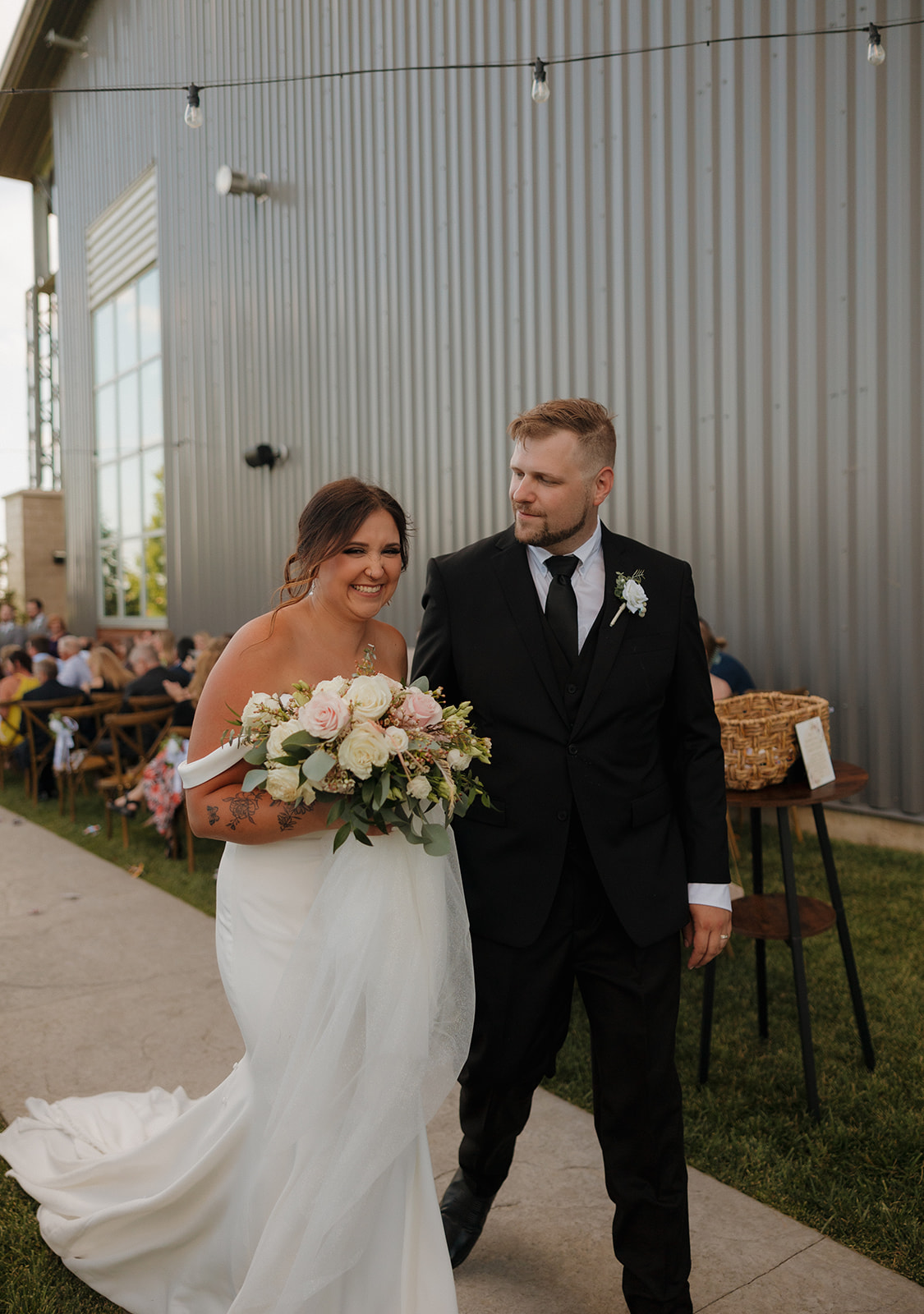 Just-married smiles as the bride and groom walk back down the aisle outside their Wisconsin brewery wedding venue, bouquet in hand.