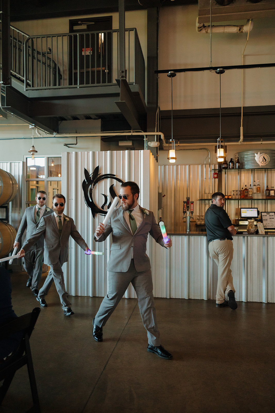 Groomsmen enter the reception with neon glow sticks and shades, hyping up the brewery dance floor with Top Gun energy.