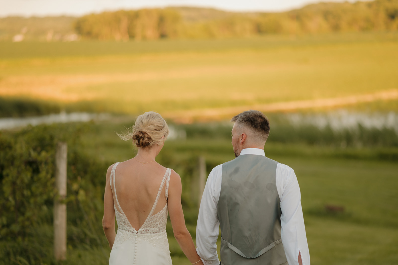 Close-up of a bride and groom walking hand-in-hand at golden hour, with rolling green hills stretching out around them.