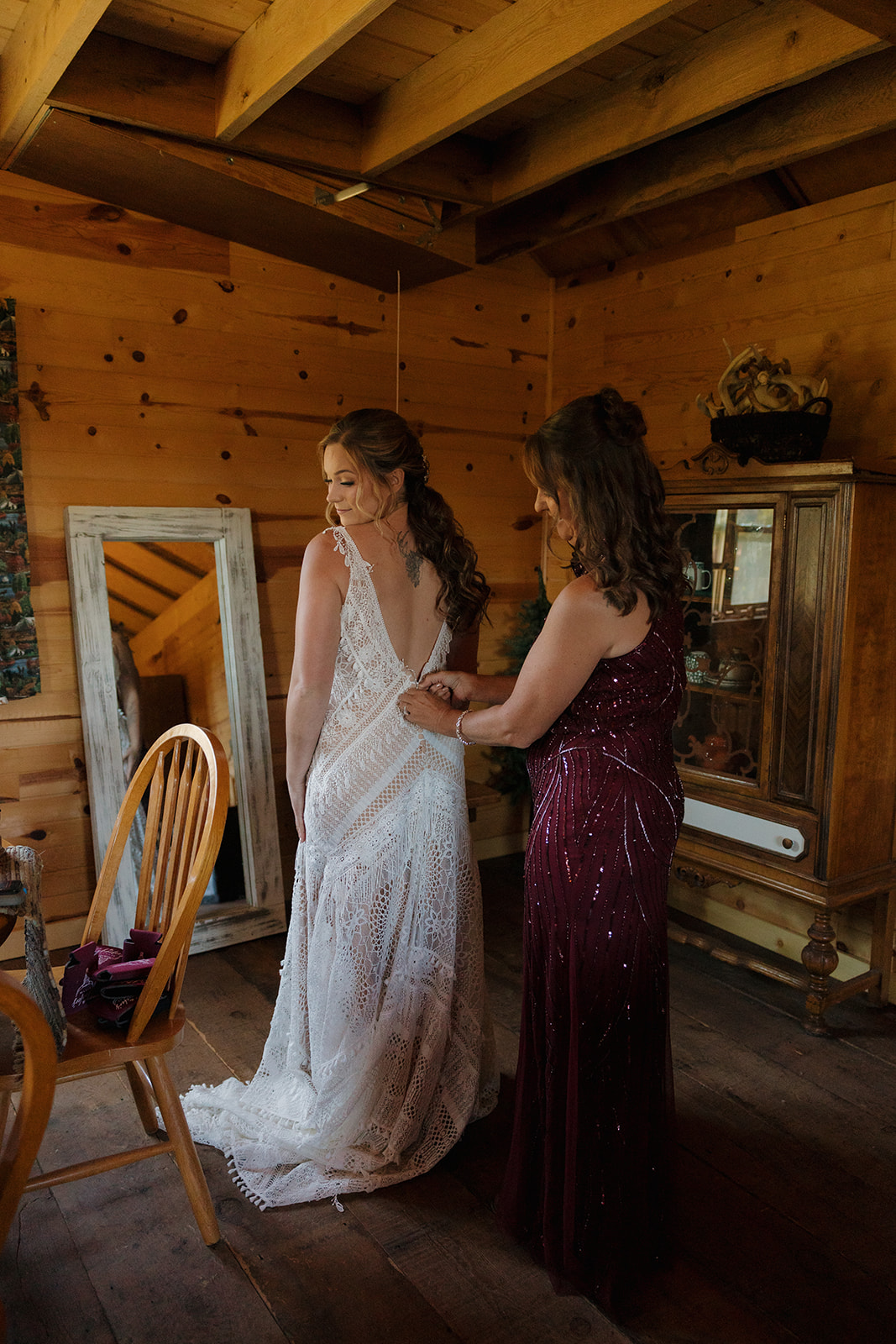 Mother helping bride into dress buttoning up the back of her gown
