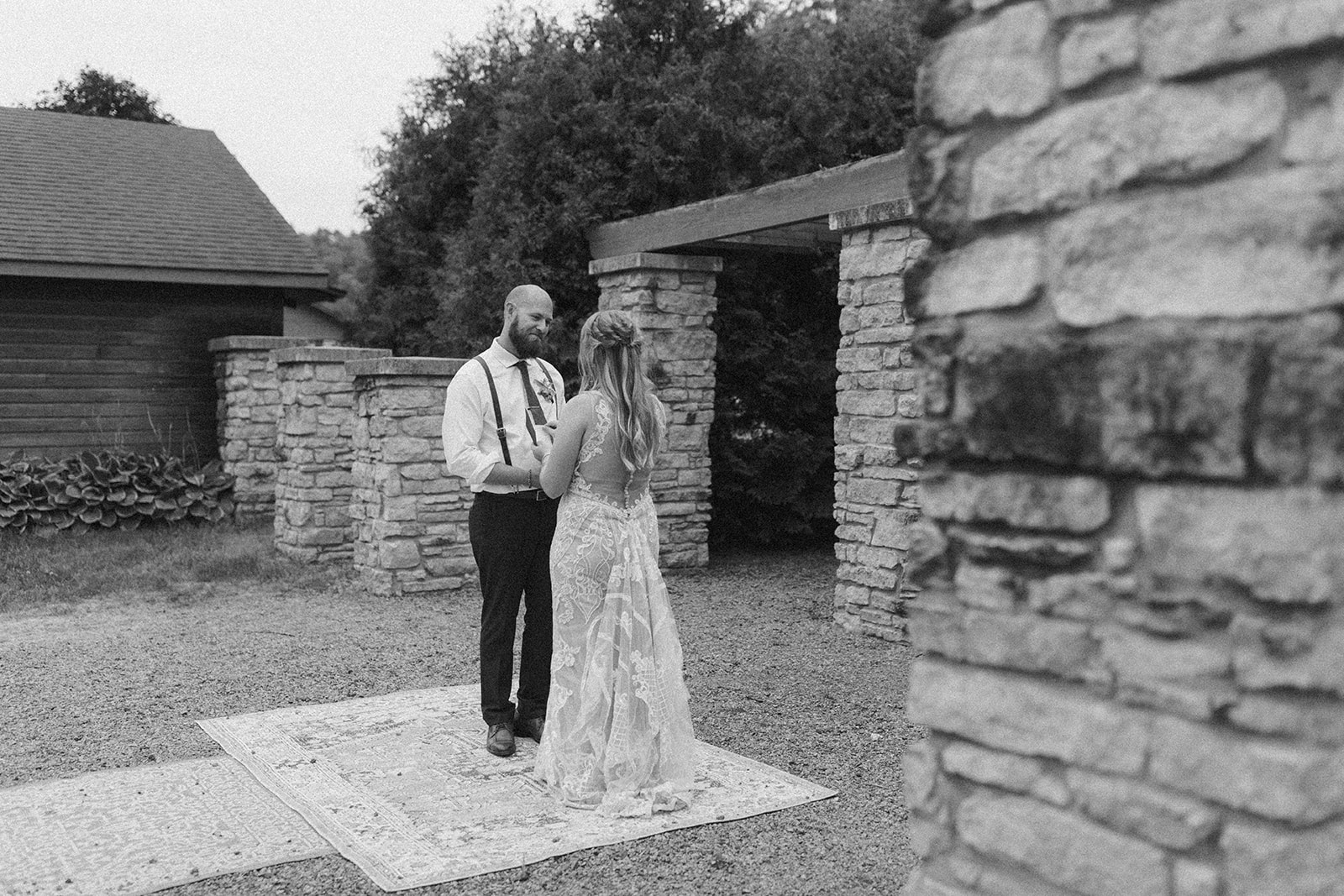 Black and white portrait of bride and groom holding hands and reading vows during private vow reading outdoors before backyard wedding in Wisconsin
