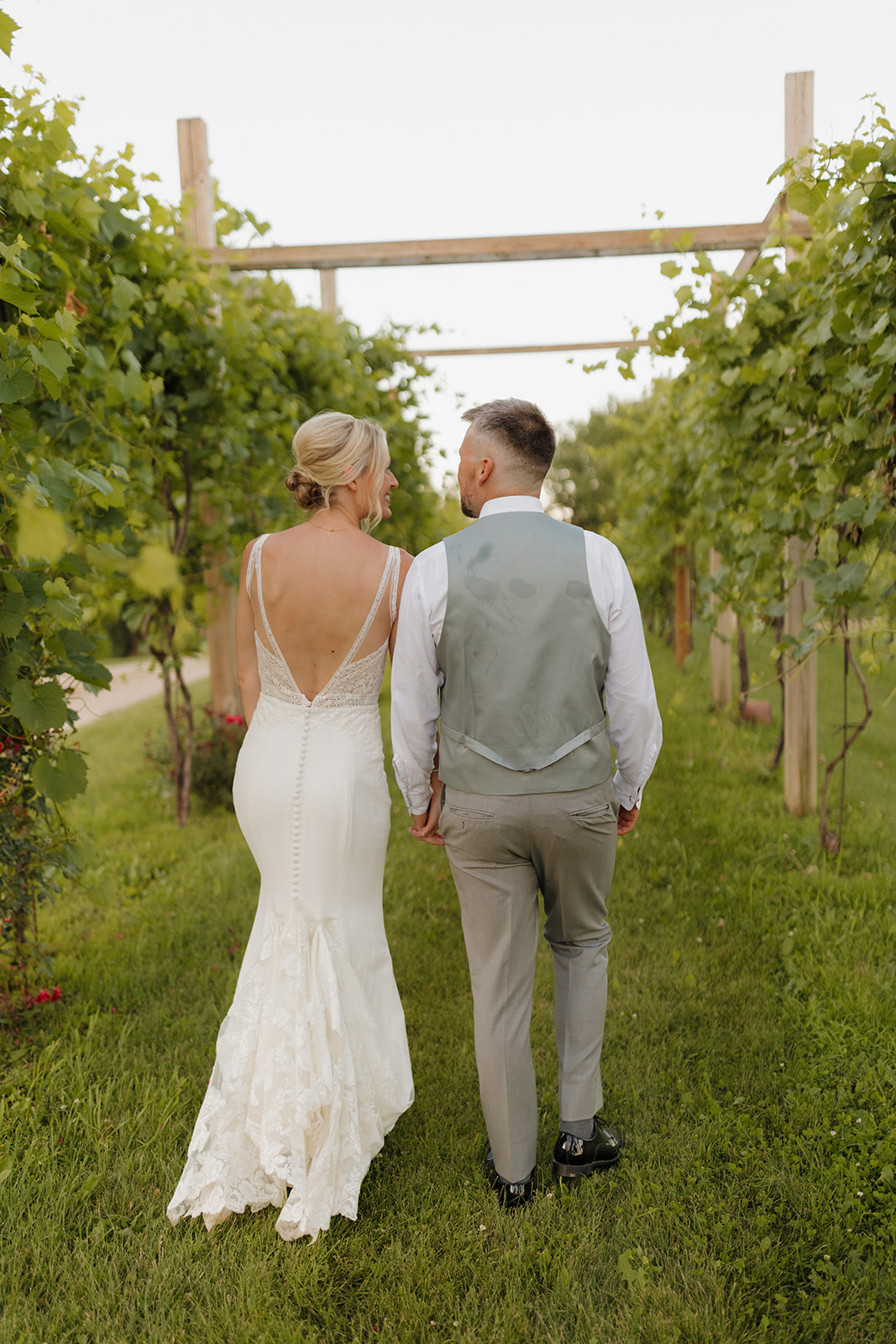 Newly married couple walk hand in hand throughout vineyard