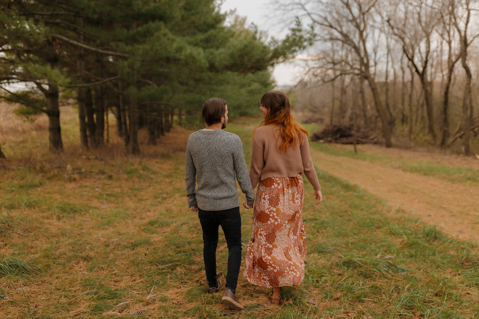 Couple strolling hand in hand through a lush green forest during their engagement photo session. 