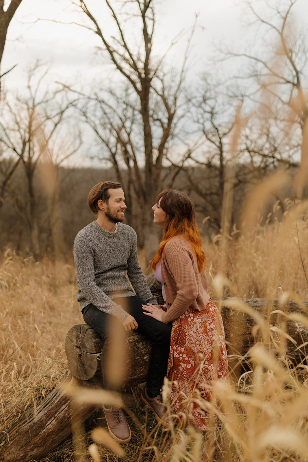 Couple sitting on a log, surrounded by tall grass, enjoying a peaceful moment together in nature.