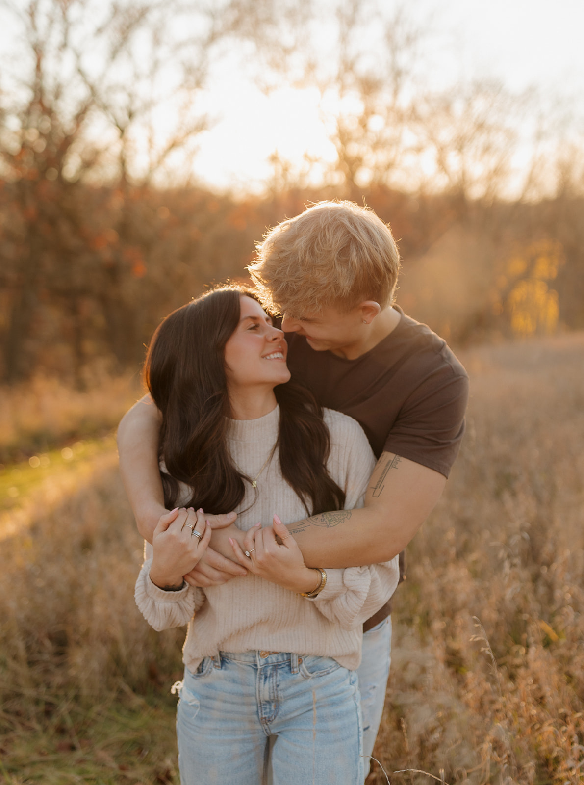 Man holding fiance from behind while touching noses with a smile on their faces at golden hour