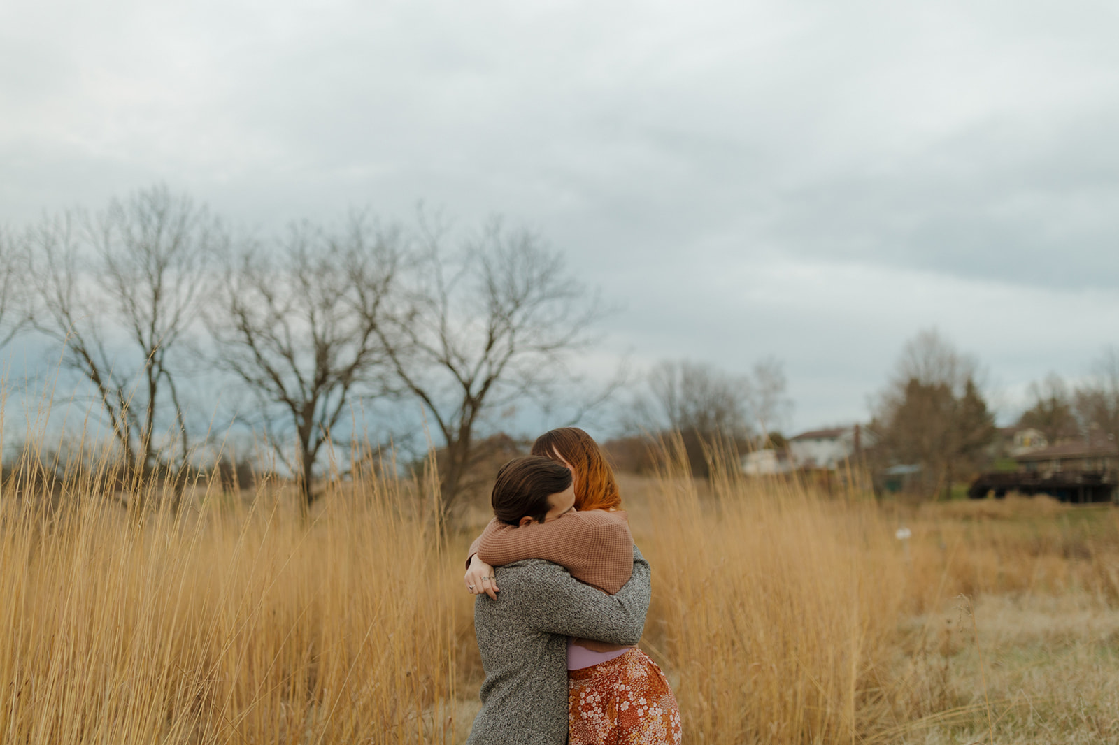 Engaged couple embrace in a tight hug in front of tall golden grass captured by madison wi wedding photographer