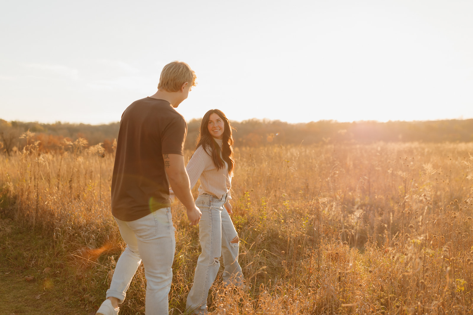 Sunset engagement session of a couple walking through tall grass, taken by a Madison WI wedding photographer.