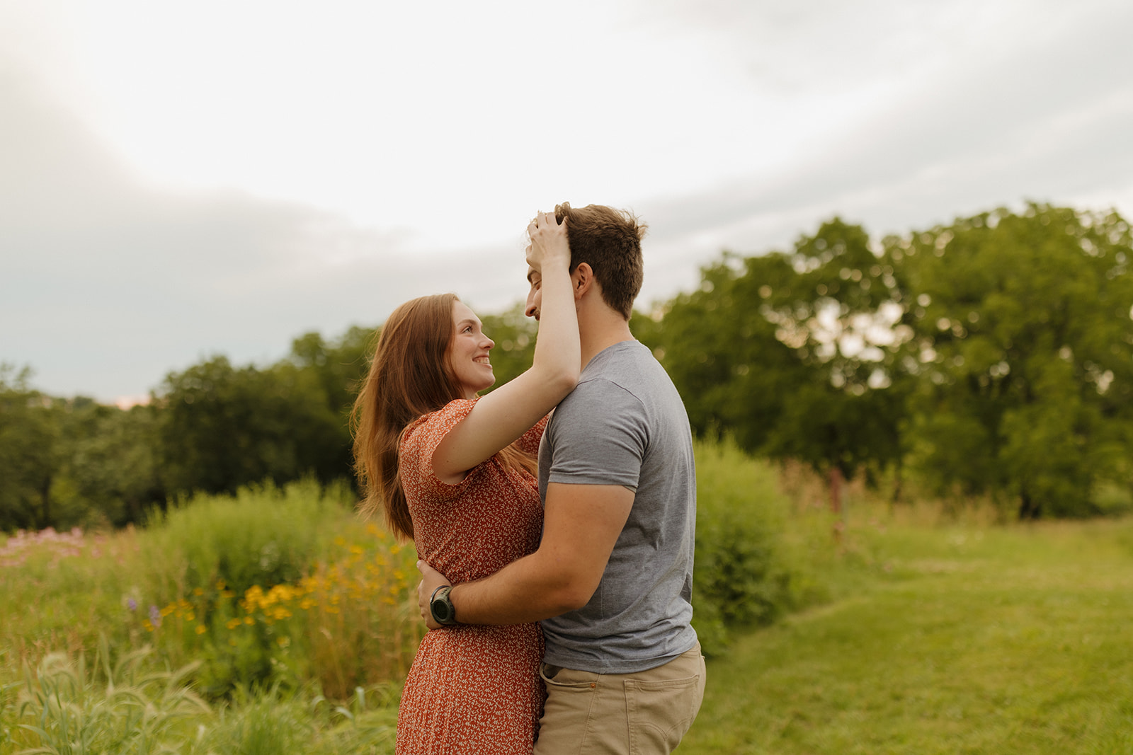 Woman pushes man's hair out of his face while he hugs her during outdoor engagement photos captured by madison wi wedding photographer