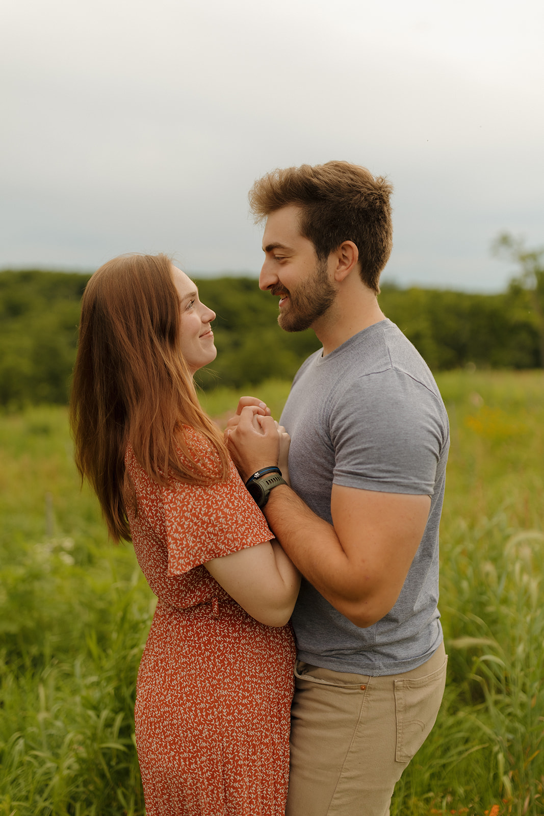 A couple standing face to face in a green meadow, holding hands and laughing as the sun sets — captured by a madison WI wedding photographer.