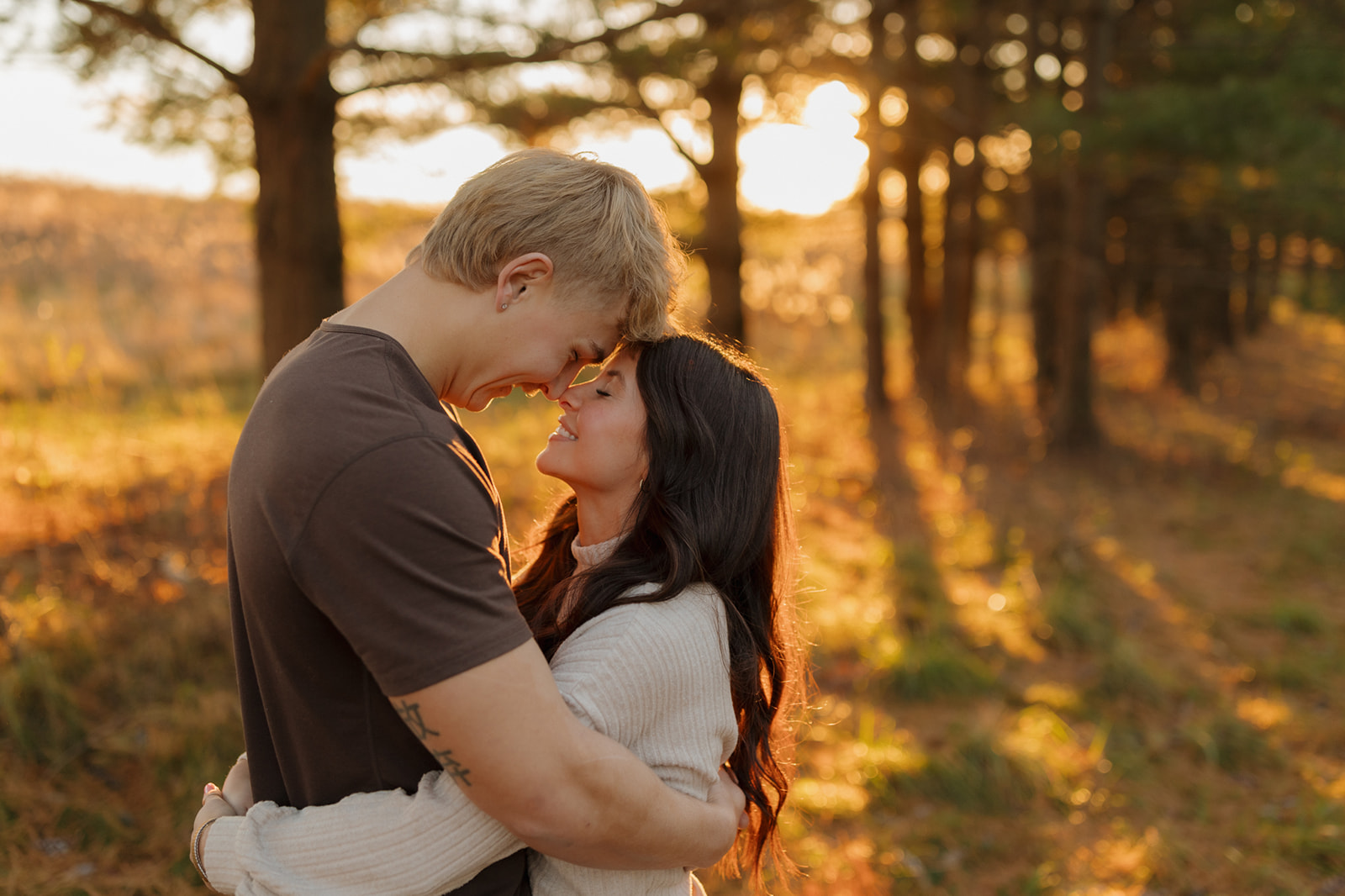 Couple embracing in a wooded area at sunset, capturing a romantic moment during their engagement session.