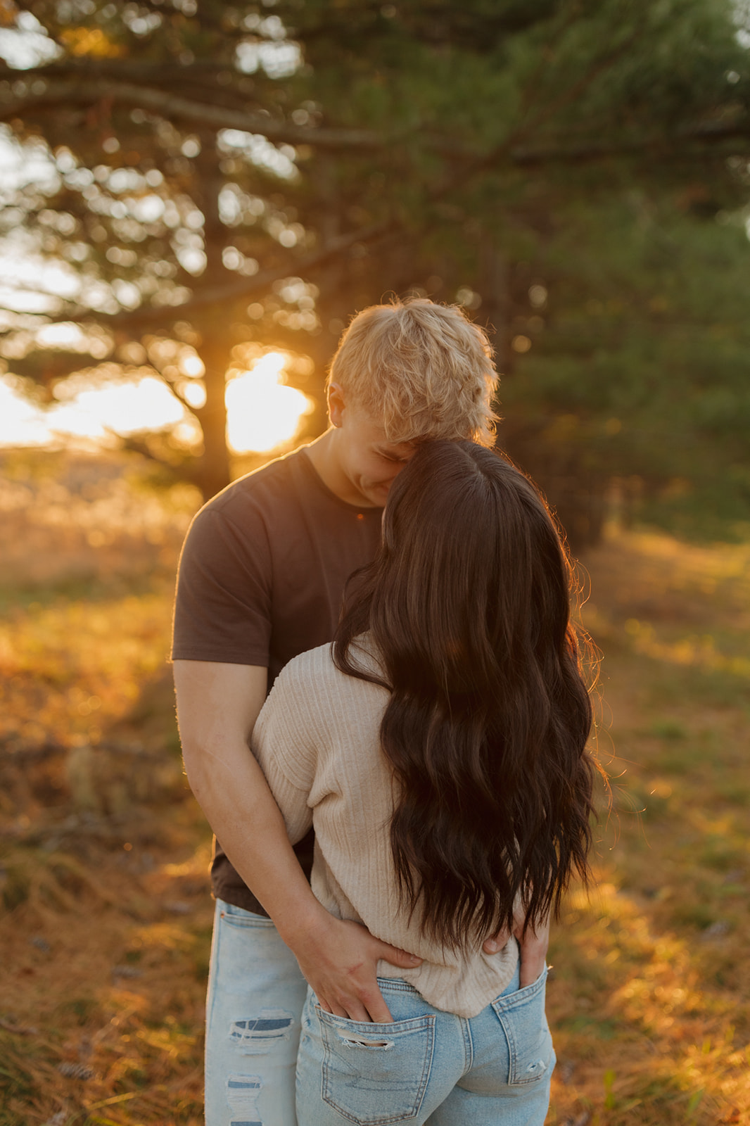 Couple embracing in a wooded area at sunset, capturing a romantic moment during their engagement session.