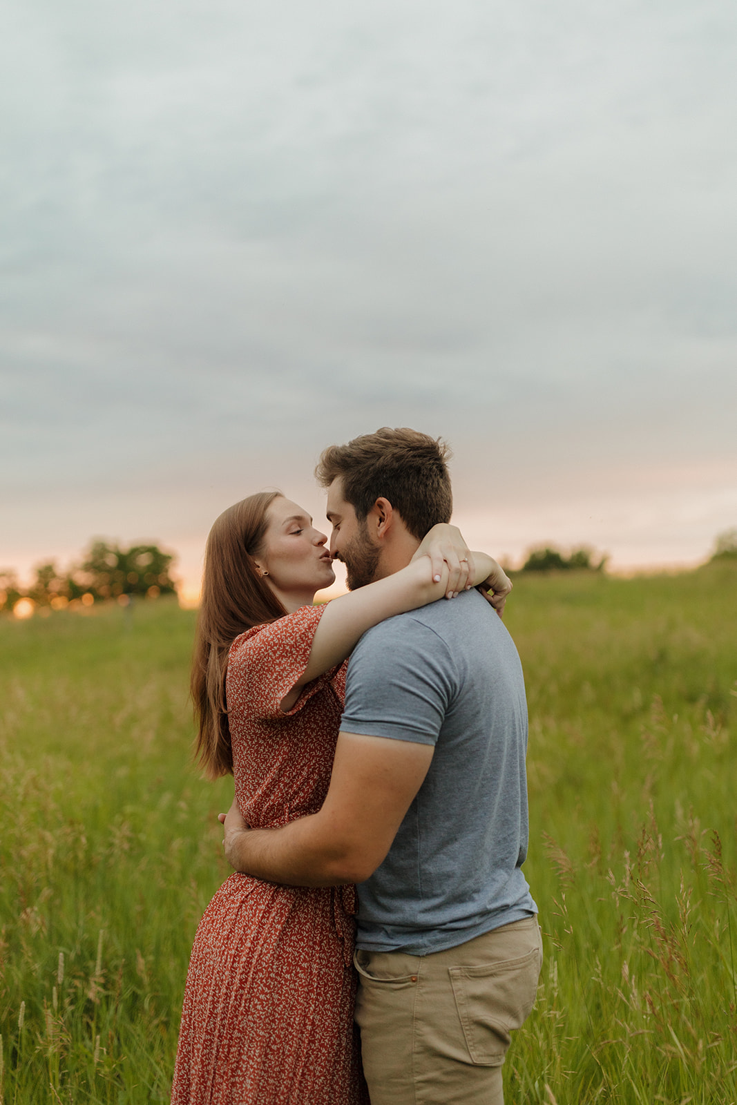 Couple sharing a kiss in a sunlit field during their engagement session at sunset.
