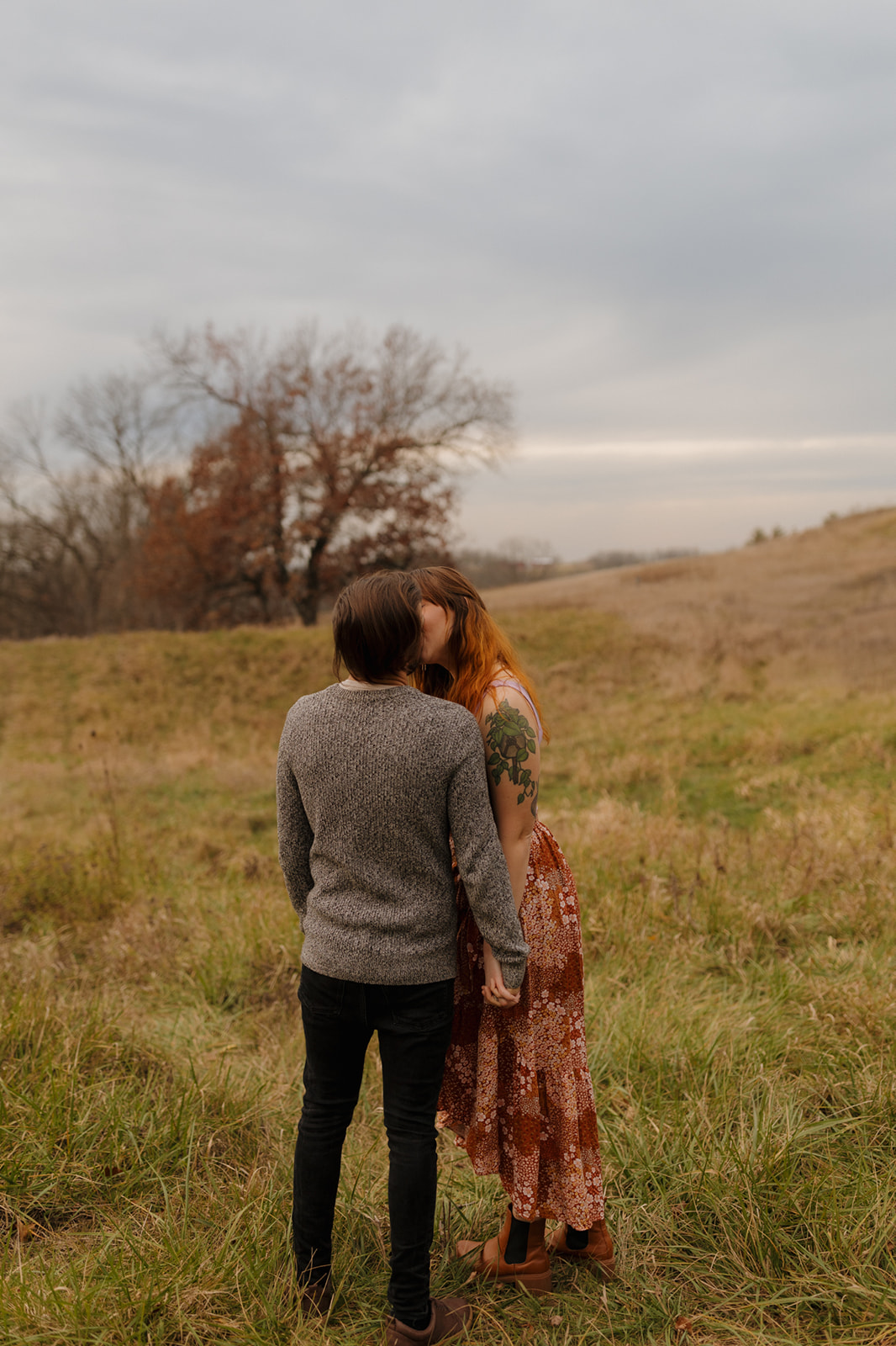 Woman leans over to kiss man during outdoor engagement photos in wisconsin at sunset captured by madison wi wedding photographer