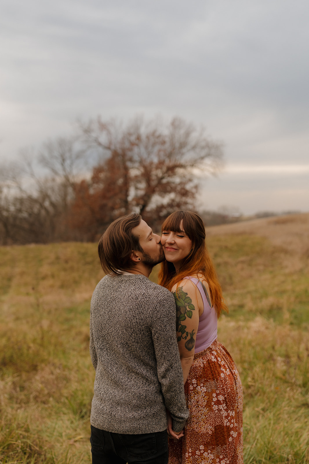 A couple sharing a kiss in a sunlit field during their engagement photo session.