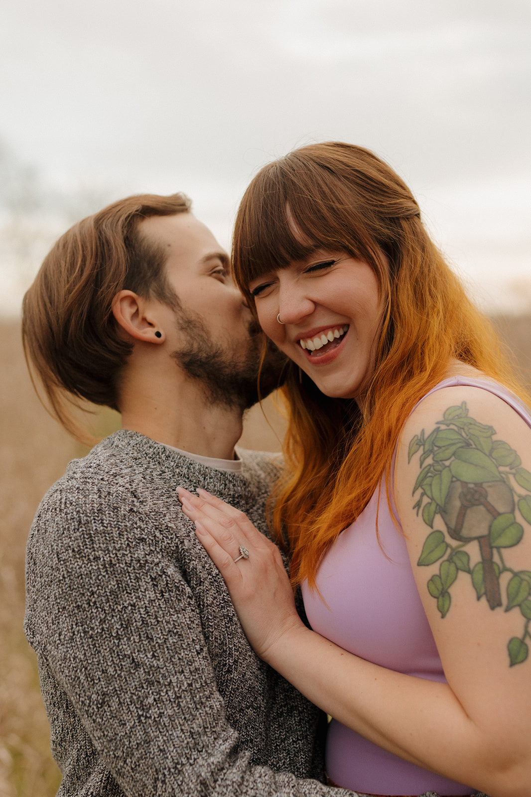 Man whispers something into woman's ear to make her laugh during outdoor engagement photos