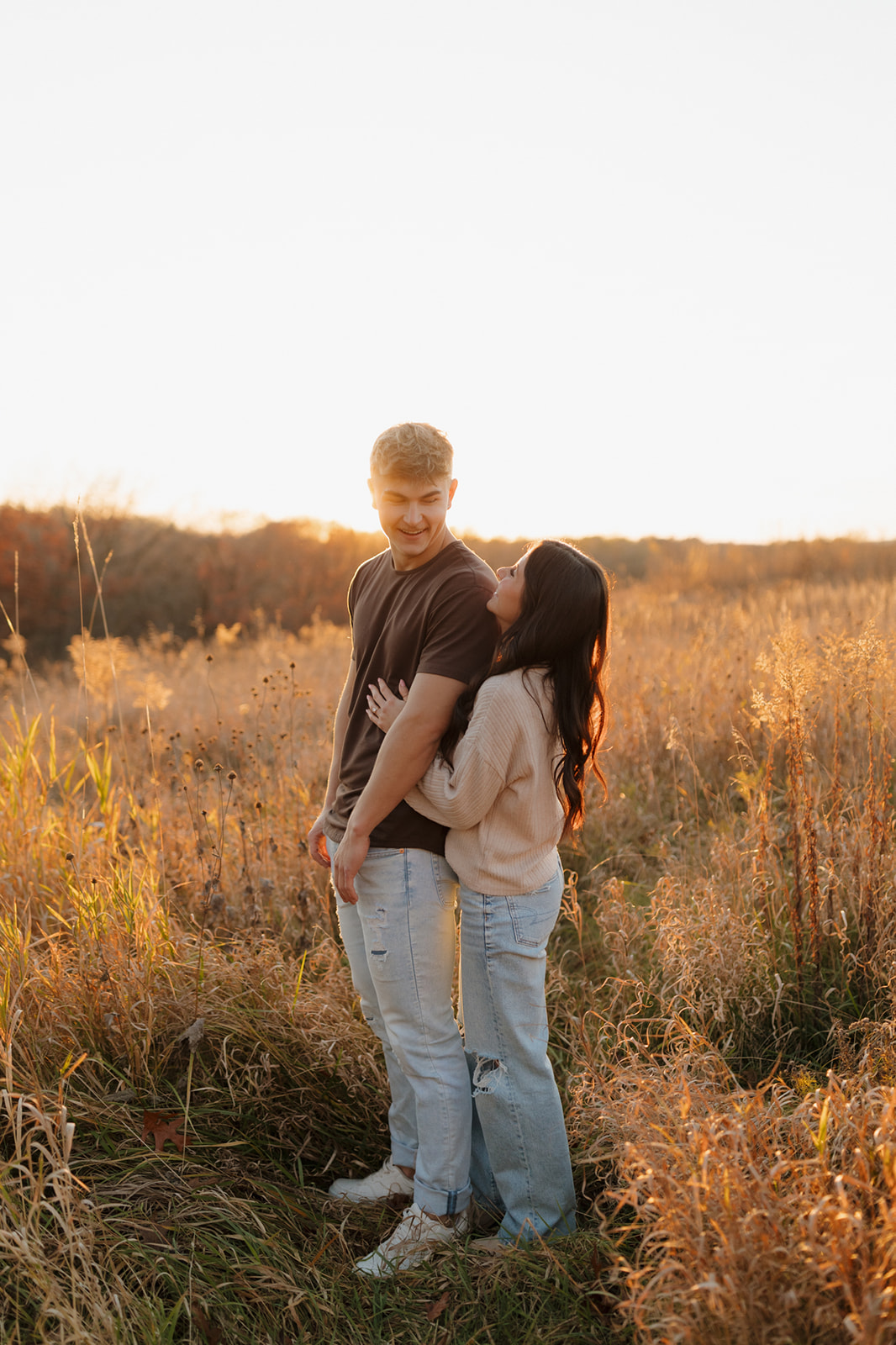 Couple embracing in a golden field during a vibrant sunset, creating a romantic and serene atmosphere.
