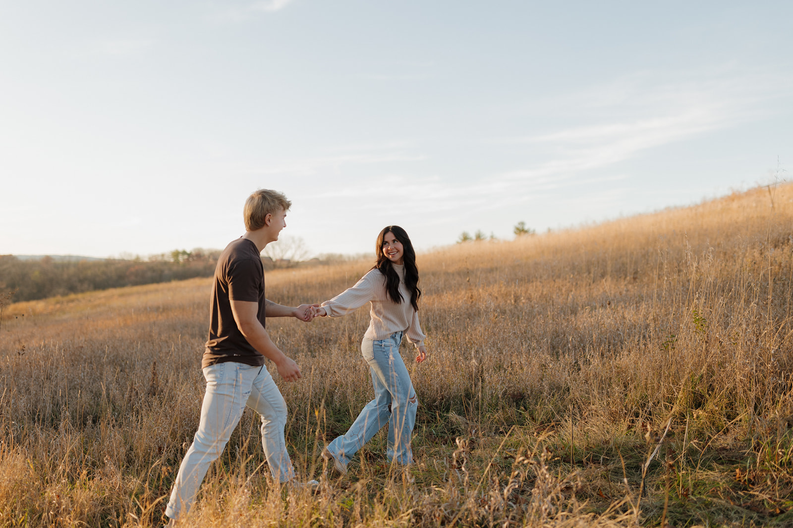 Woman leads man into golden field of grass during outdoor engagement photos in wisconsin