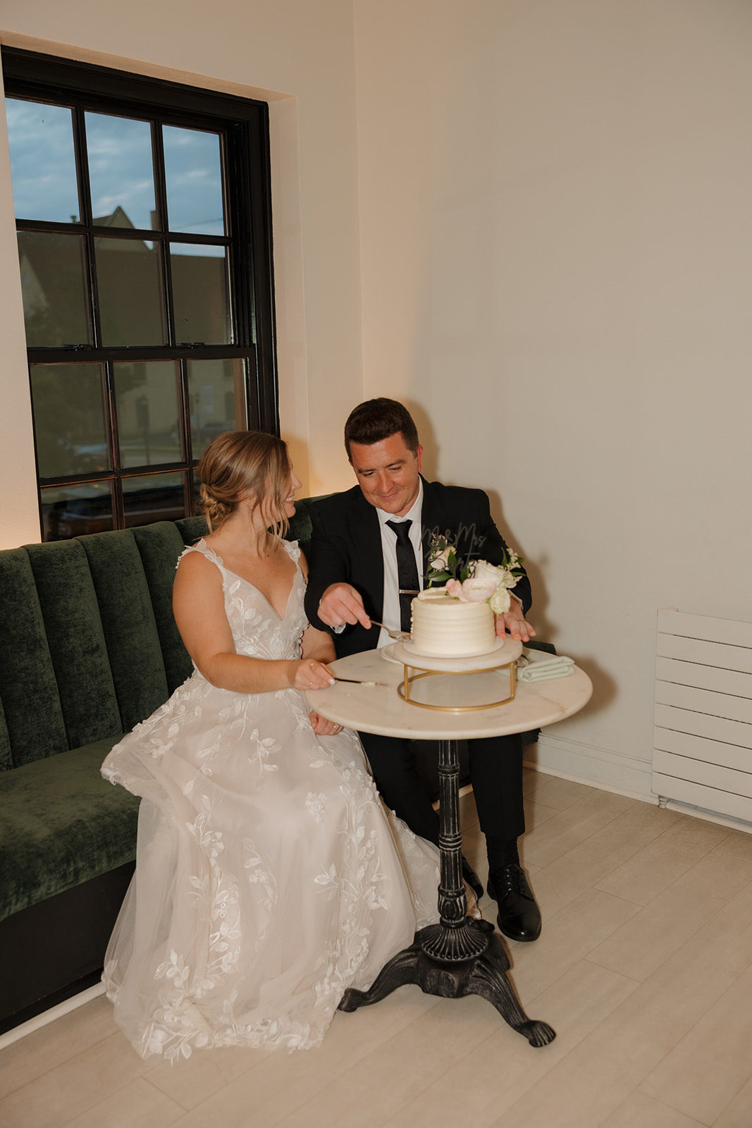 Bride and groom sit together in private corner of their reception to cut wedding cake as newly married couple