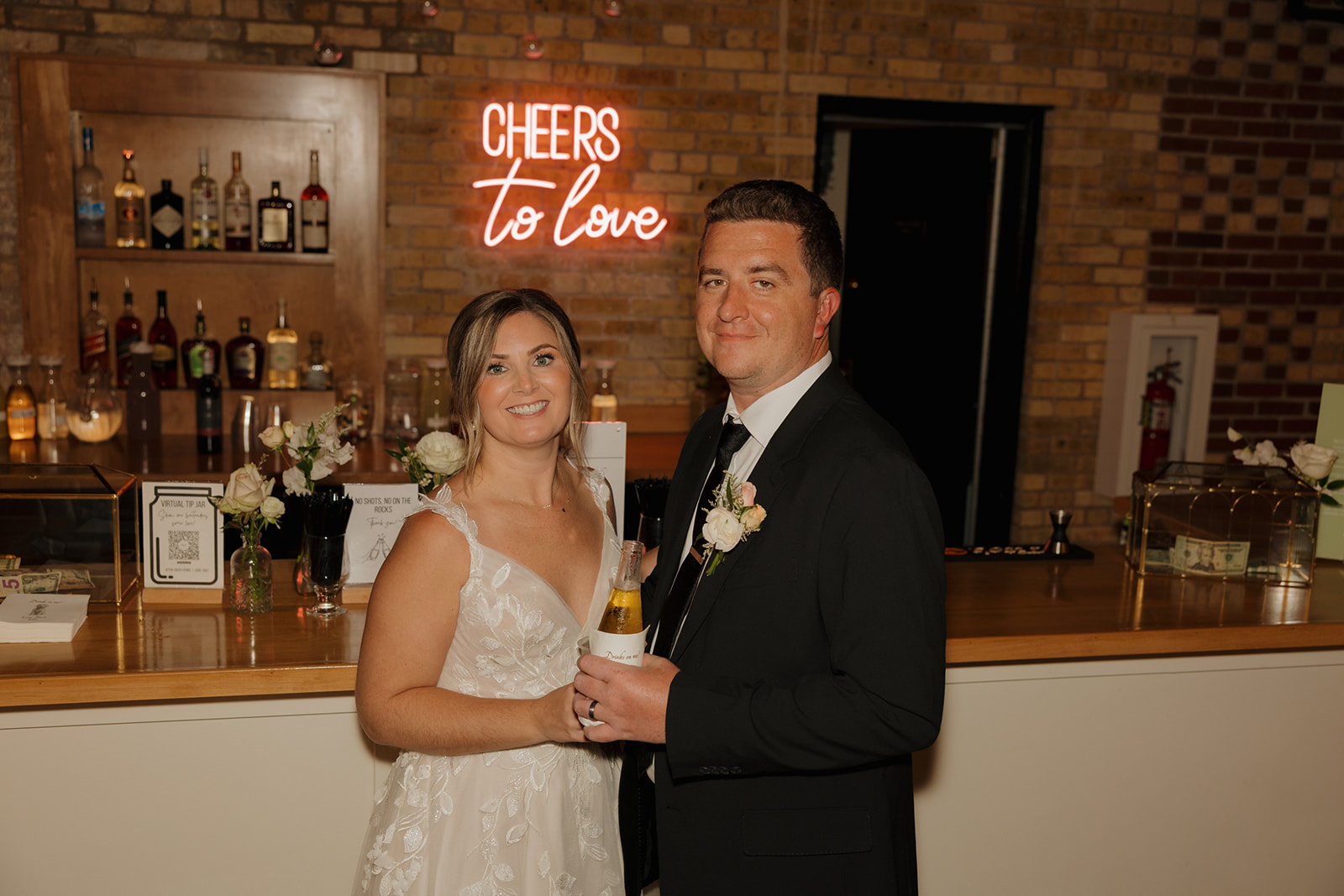 The bride and groom pose happily in front of a bar, capturing a joyful moment on their wedding day.
