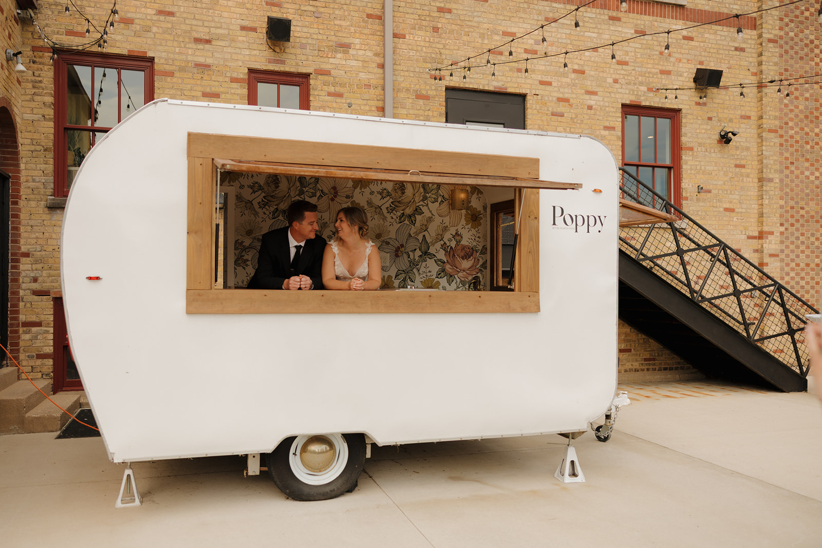 A bride and groom happily pose together inside a charming vintage trailer, surrounded by rustic decor.

