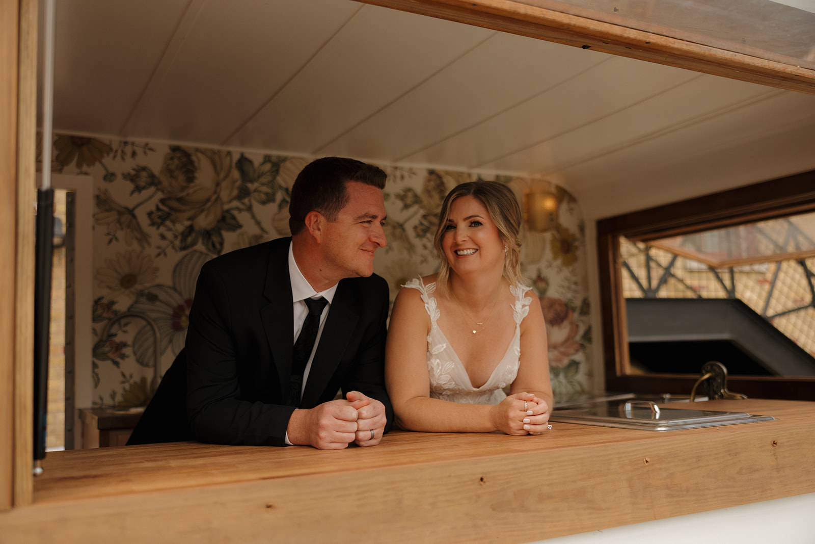 Groom looks over at his bride while they stand inside mobile food trailer at 10 South wedding venue in Wisconsin