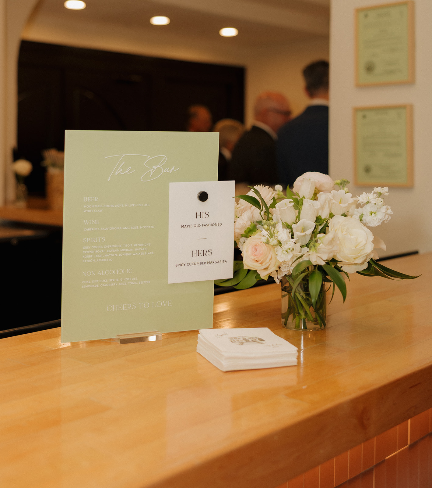 Green bar signs showing signature drinks for the evening with white flowers beside them