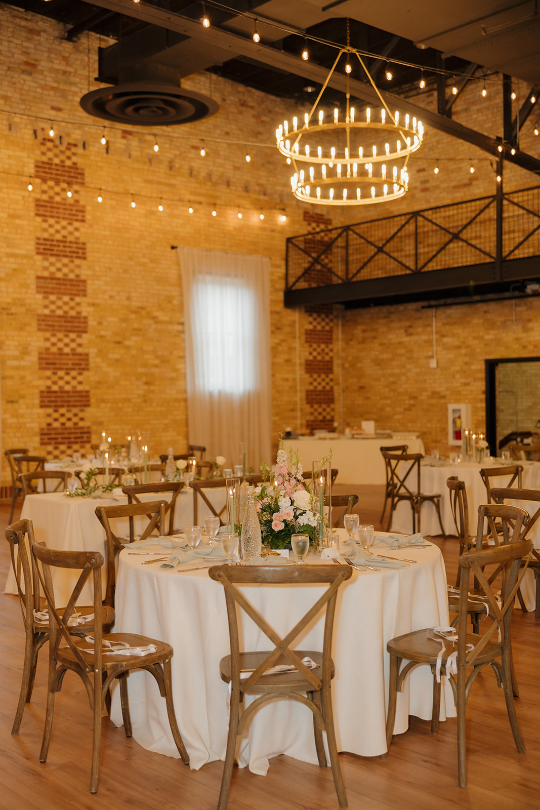 Indoor wedding reception with tables covered in white table cloths, and decorated with silverware and florals