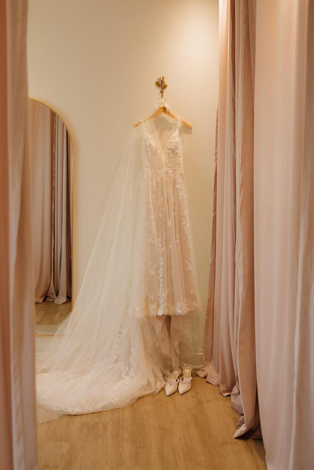 Lace wedding dress hanging on personalized hanger with white bridal shoes below it before wedding ceremony