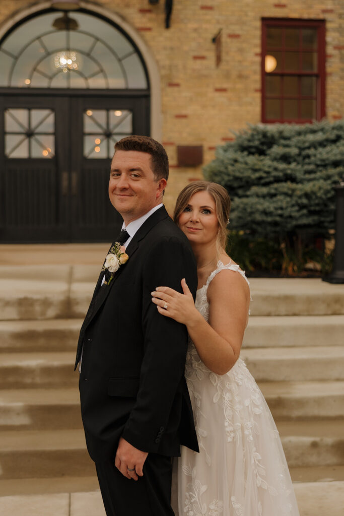 Bride holding groom's arm and hugging him from behind in wedding attire at 10 South wedding venue in Wisconsin