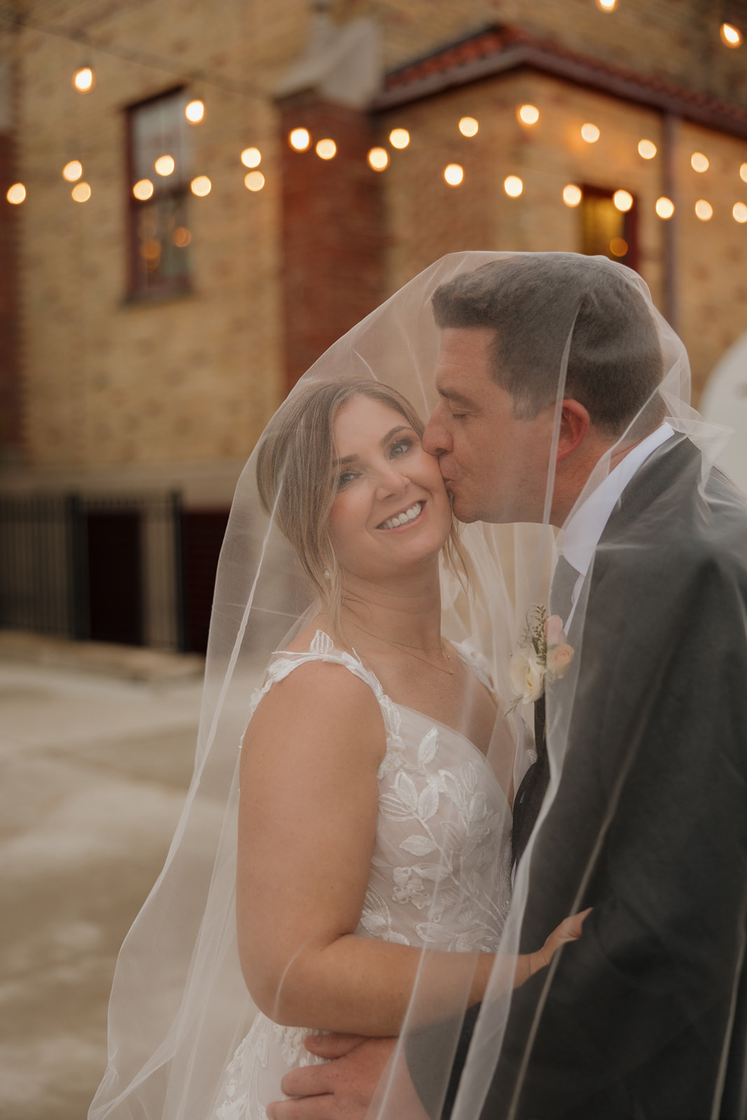 A bride and groom share a kiss under a veil capturing a romantic moment.
