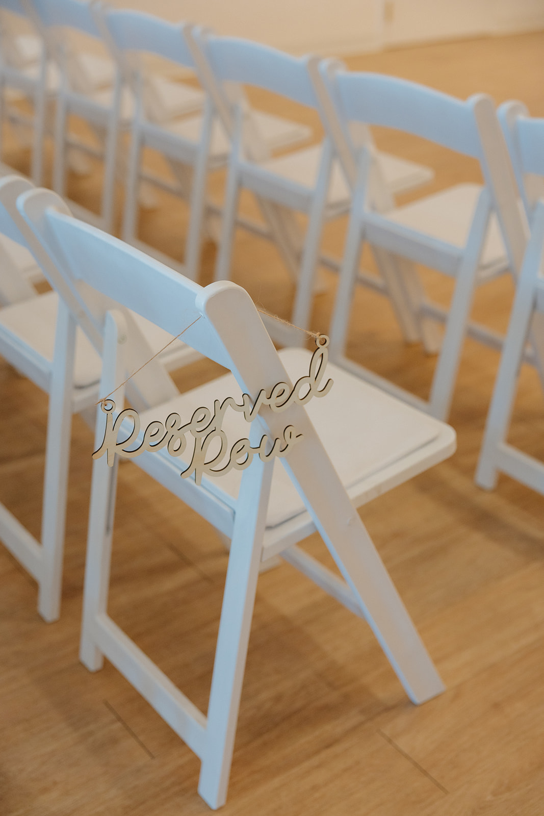 Close-up of a white folding chair with a gold “Reserved Row” sign hanging from the back, adding a thoughtful touch to the ceremony setup.