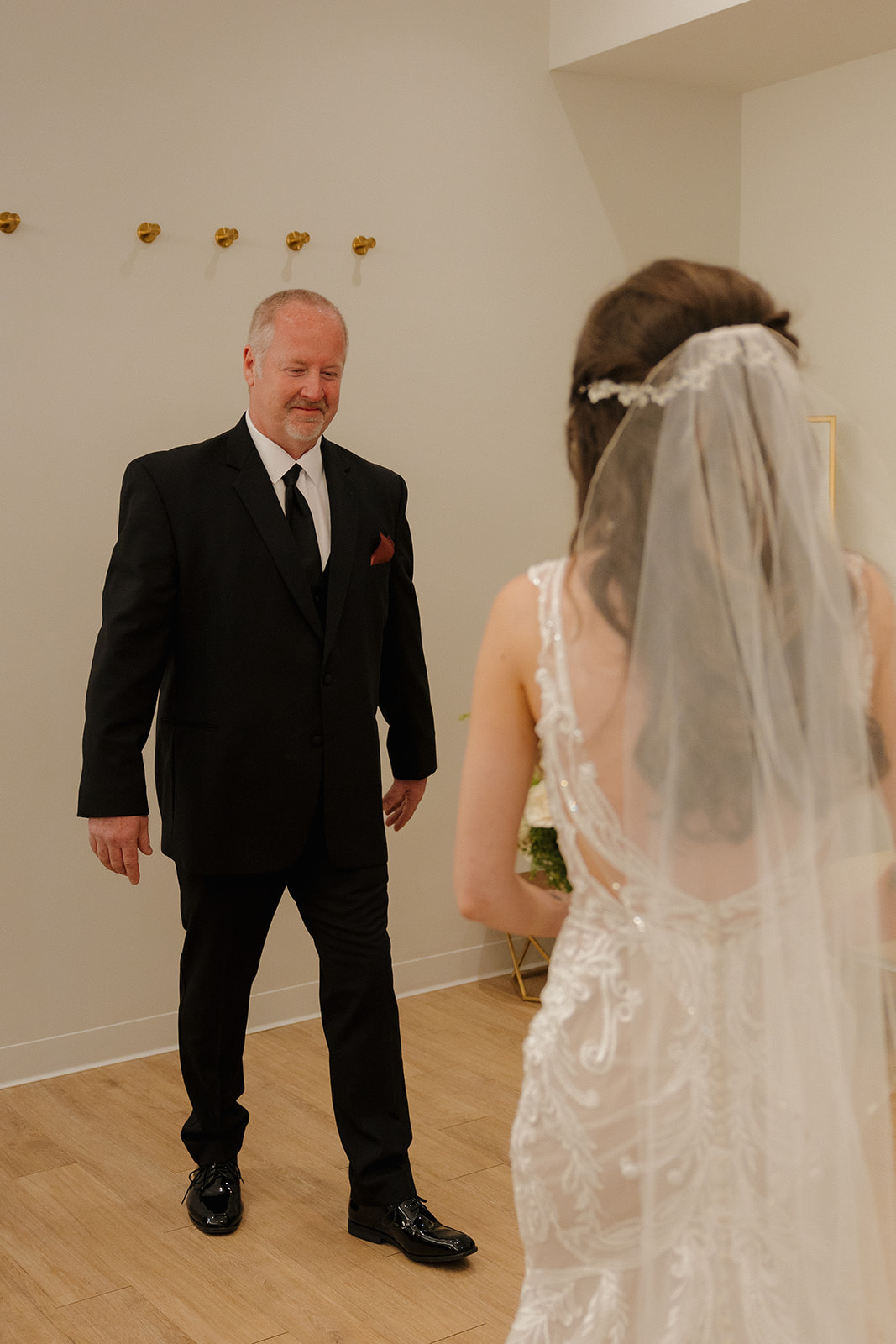 Father of the bride walks in with a proud, emotional smile as he sees his daughter in her gown for the first time.