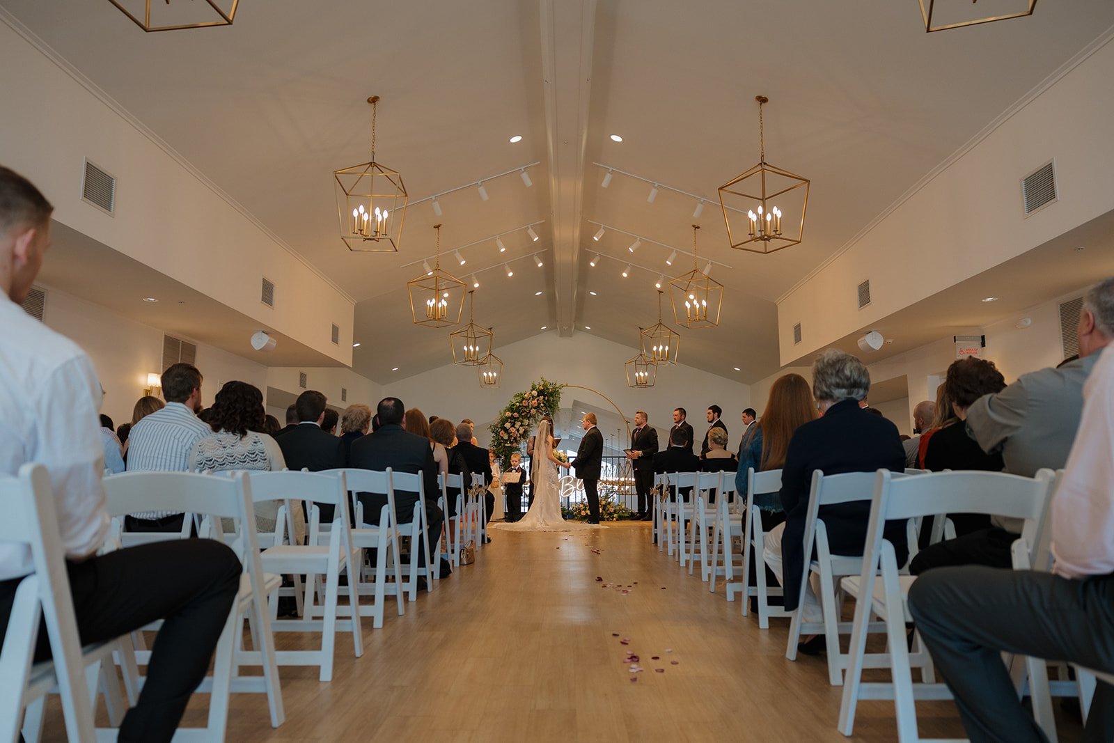 Guests watch as the couple exchanges vows under a floral hoop arch in a bright, modern ceremony space—captured by a madison wedding photographer.