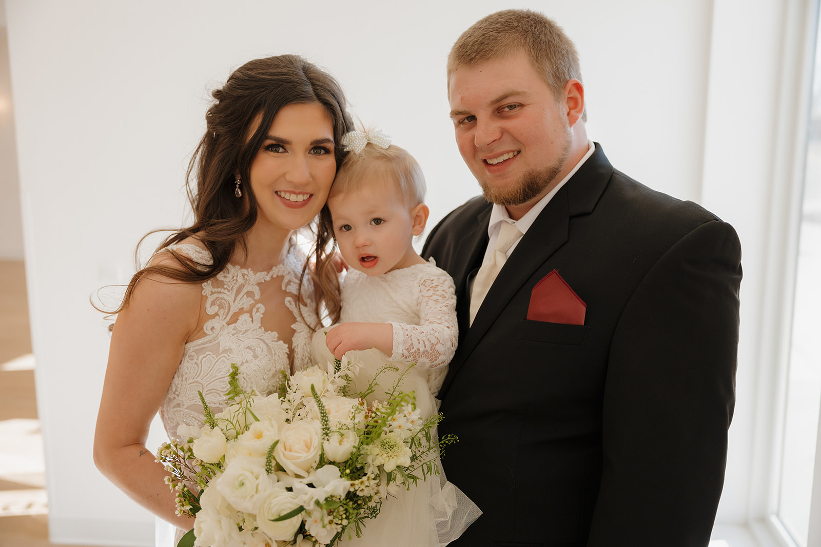Bride and groom pose with their daughter, all glowing in natural light—madison wedding photographer captures the joy and love.
