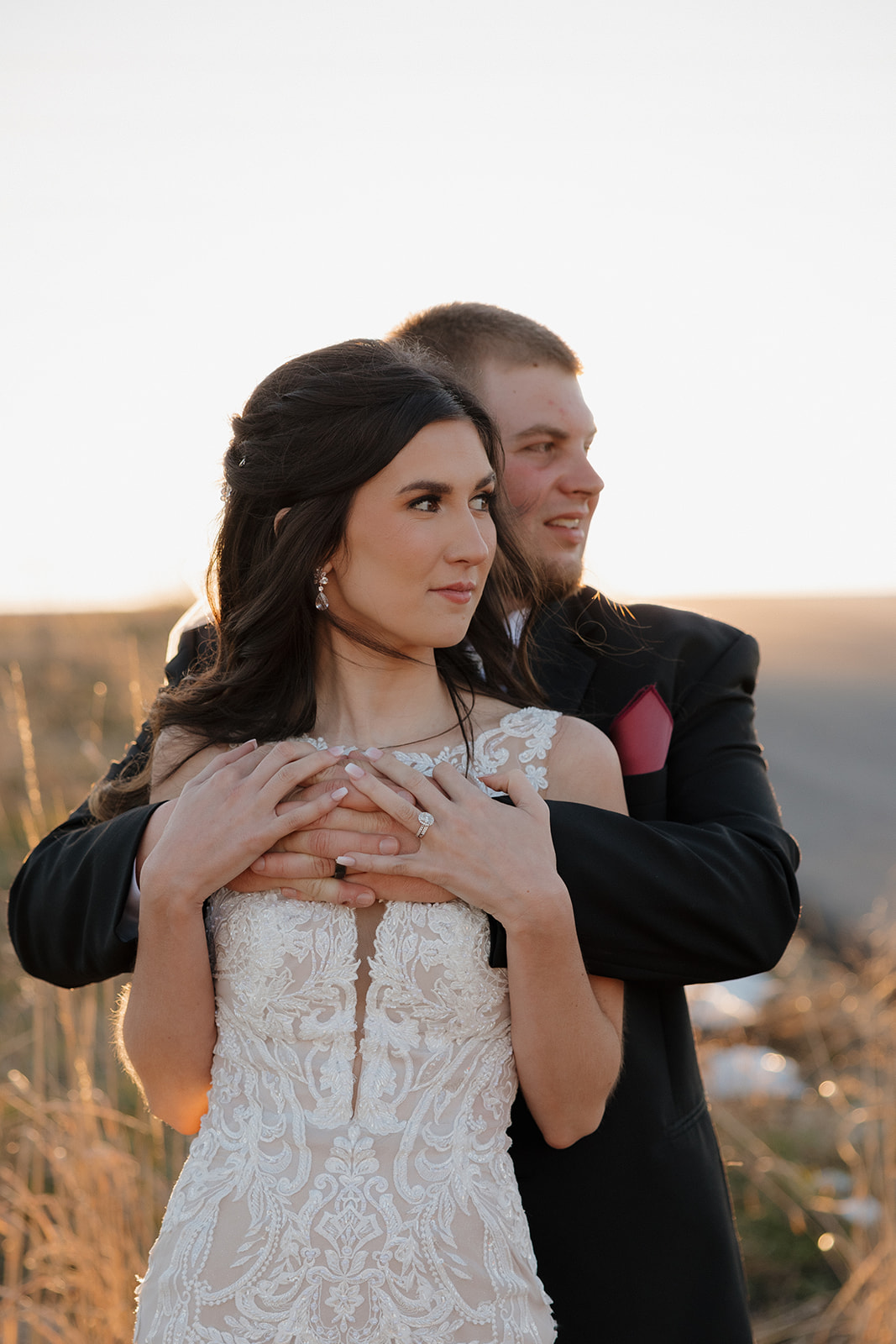 Groom wraps his arms around the bride from behind as golden light streams in—classic romance with a soft, modern edge.
