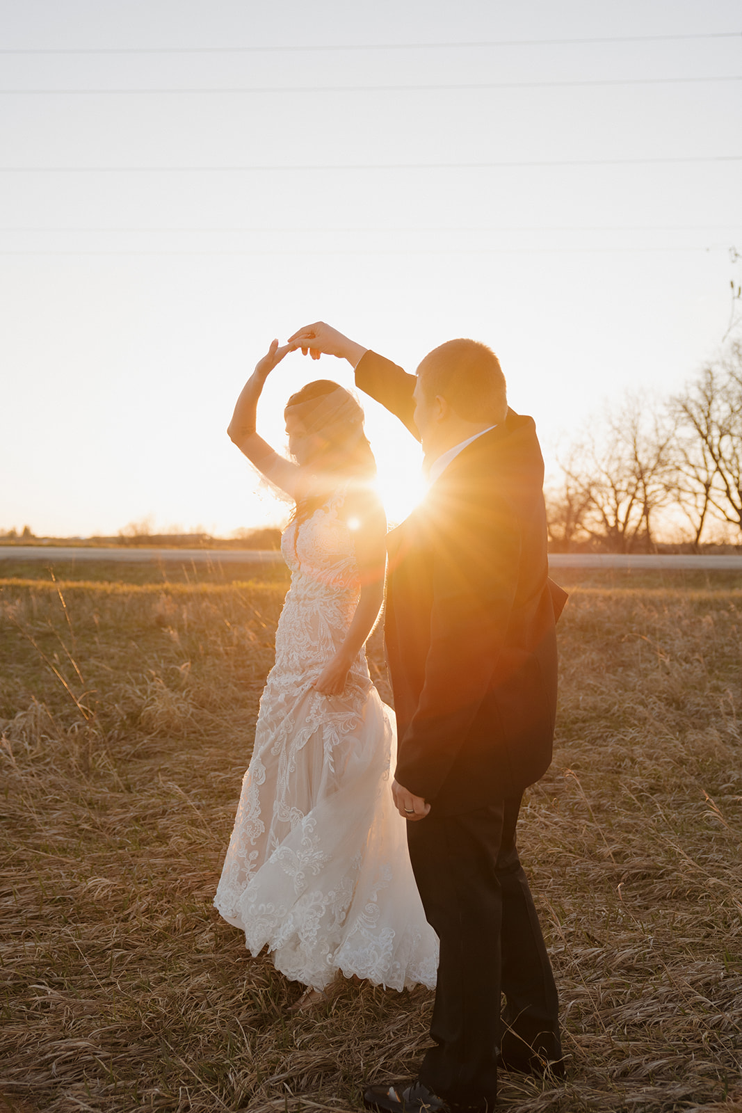 Groom twirls the bride in a sunlit field as the setting sun flares between them—captured perfectly by a madison wedding photographer.