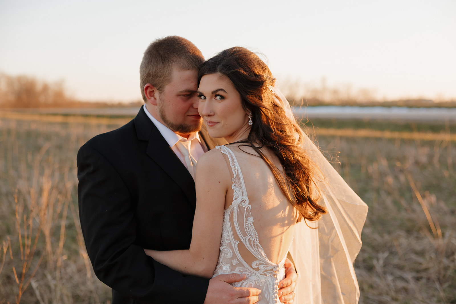 Bride gazes over her shoulder as groom holds her close, with her veil catching the light—madison wedding photographer captures the intimate vibes.