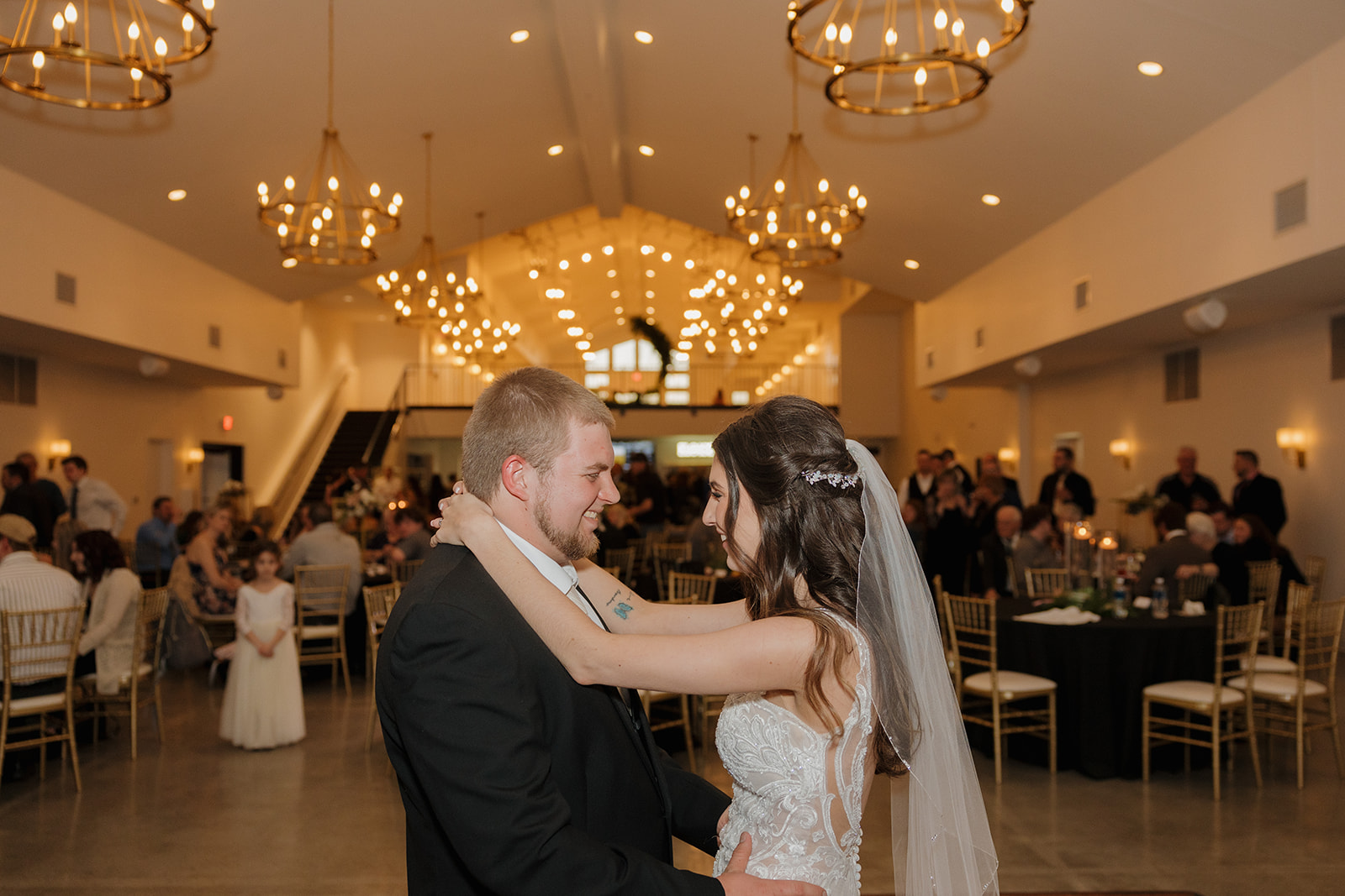 Bride and groom share their first dance under glowing chandeliers as guests watch from their seats—madison wedding photographer captures the magic.