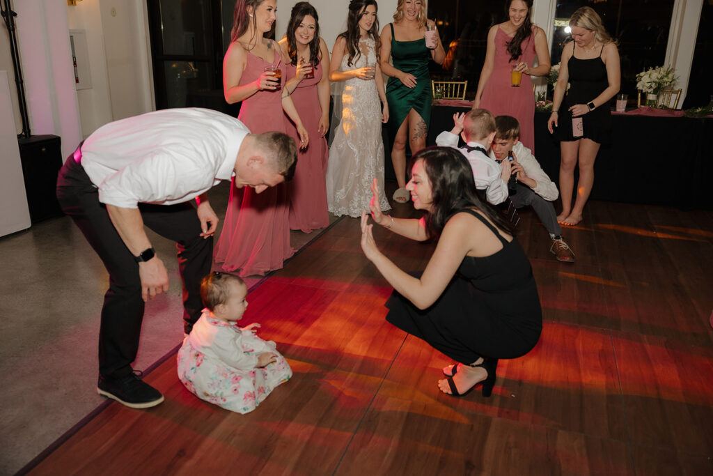 A toddler sits on the dance floor while guests cheer her on—this madison wedding photographer moment captures the cutest impromptu party starter.