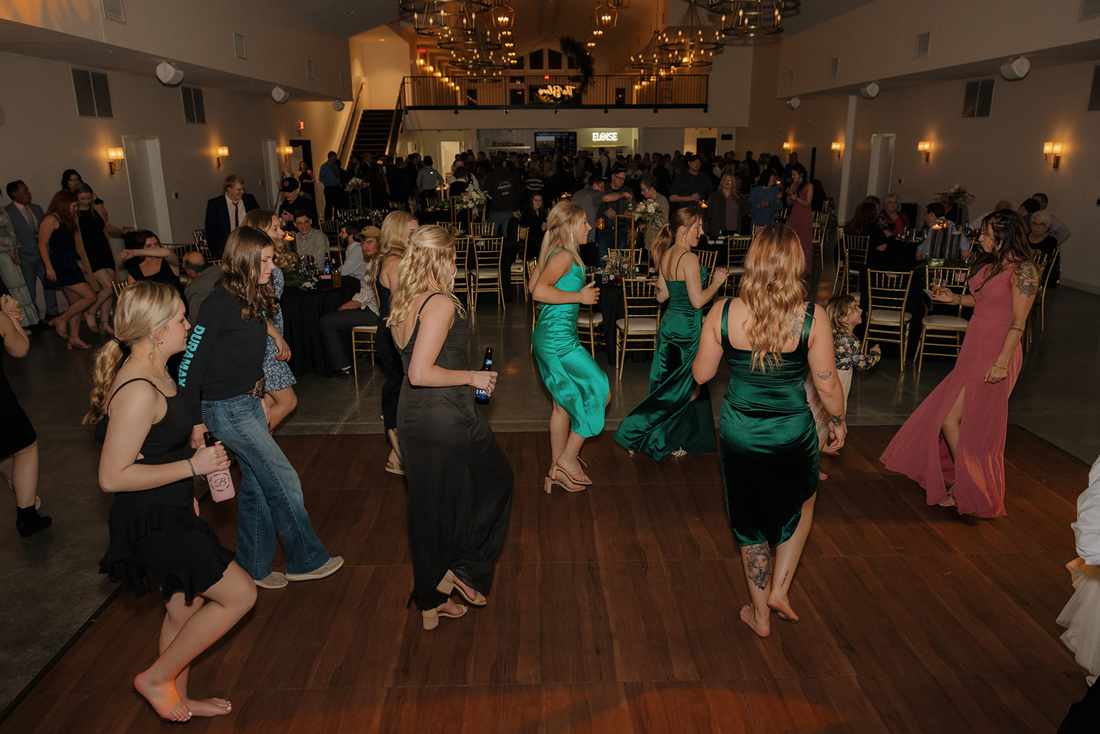 Guests hit the dance floor in cocktail dresses and heels under warm chandeliers, bringing the energy to the wedding reception.