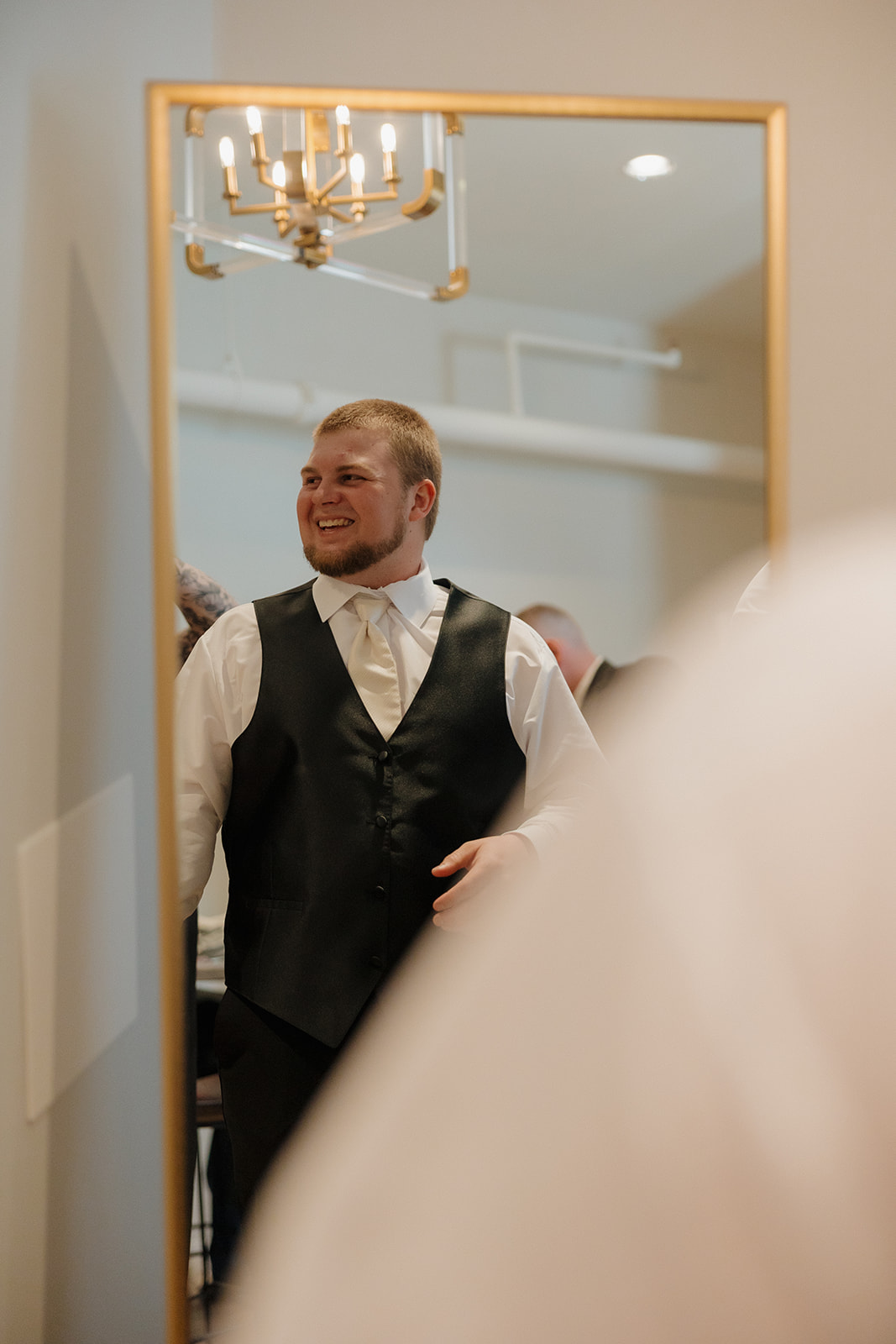 Groom smiles at himself in a gold-framed mirror, ready to walk down the aisle—madison wedding photographer captures the quiet confidence.