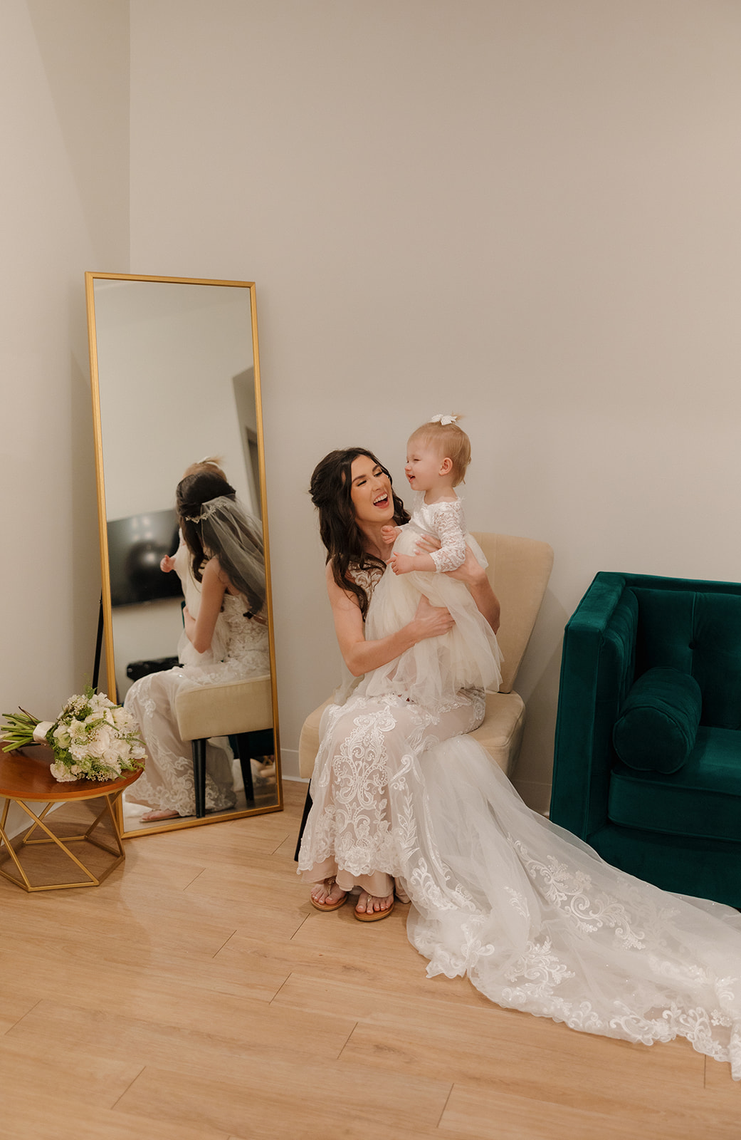 Bride sits in the getting ready suite holding her toddler daughter, both beaming in a quiet, sweet pre-ceremony moment—madison wedding photographer captures the heart of it all.